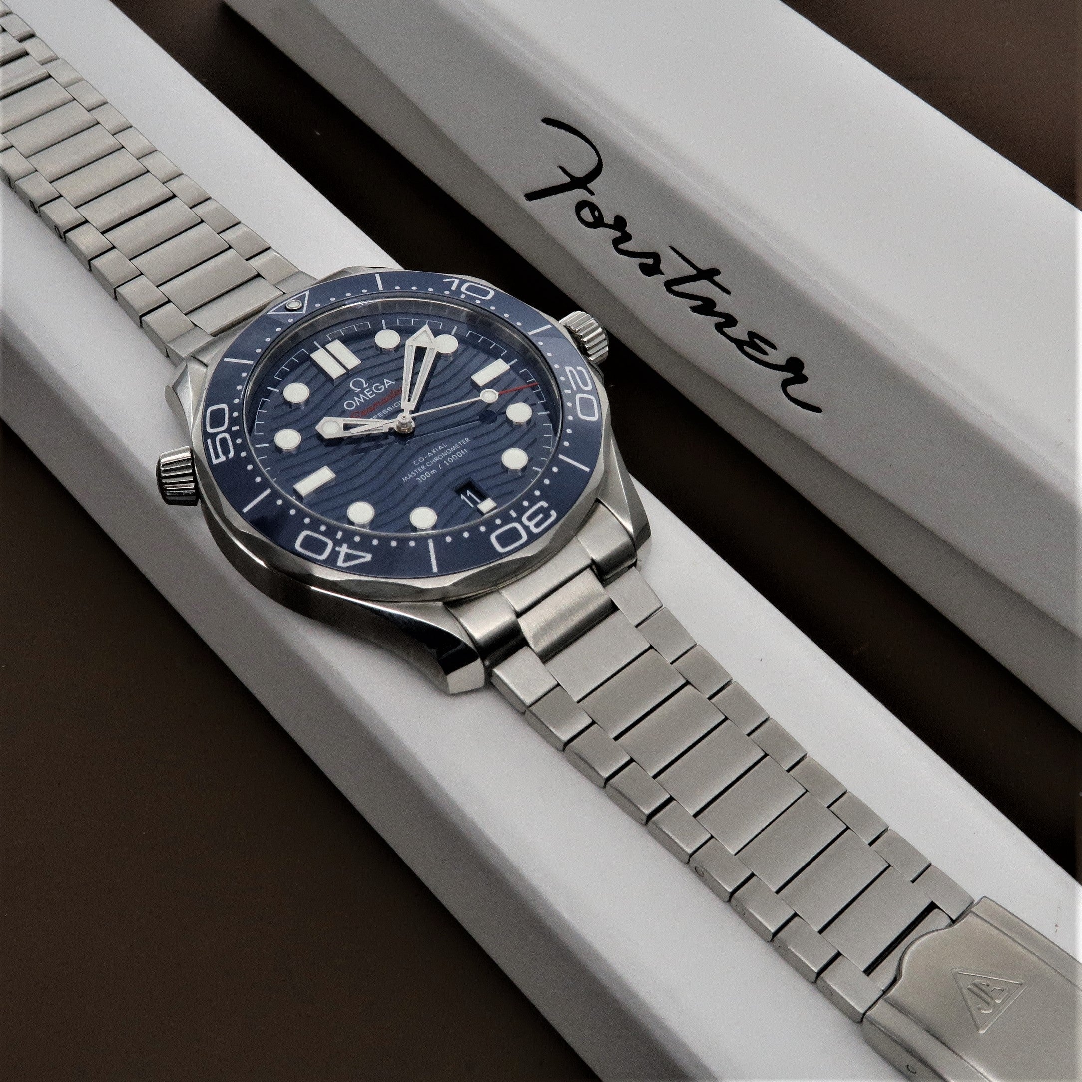Omega Seamaster dive watch with blue dial and steel bracelet on white display box with Forstner branding