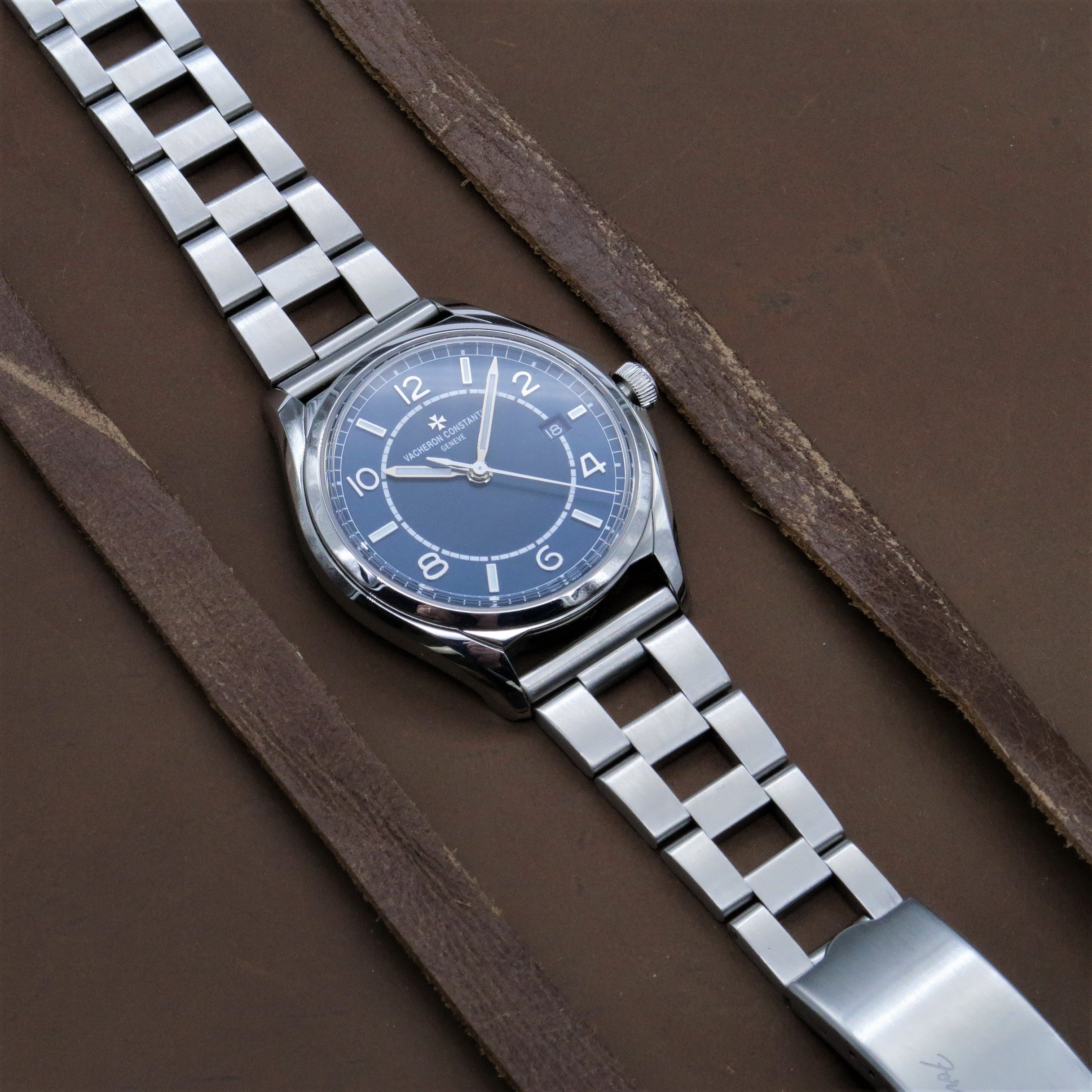 Silver stainless steel watch with blue dial and ladder-style bracelet on brown wood background