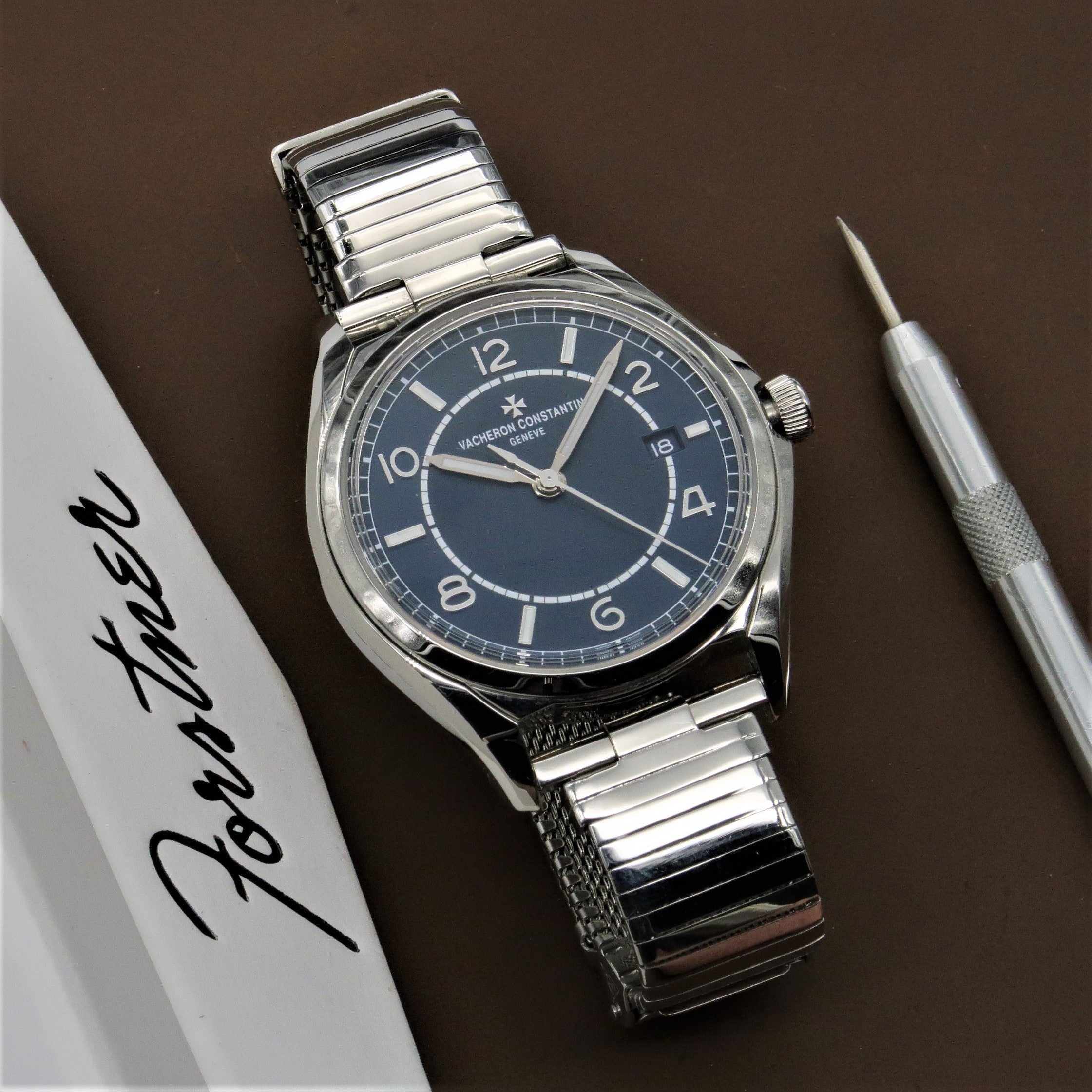 Vacheron Constantin stainless steel watch with dark blue dial, applied numerals, and expandable metal bracelet on brown background