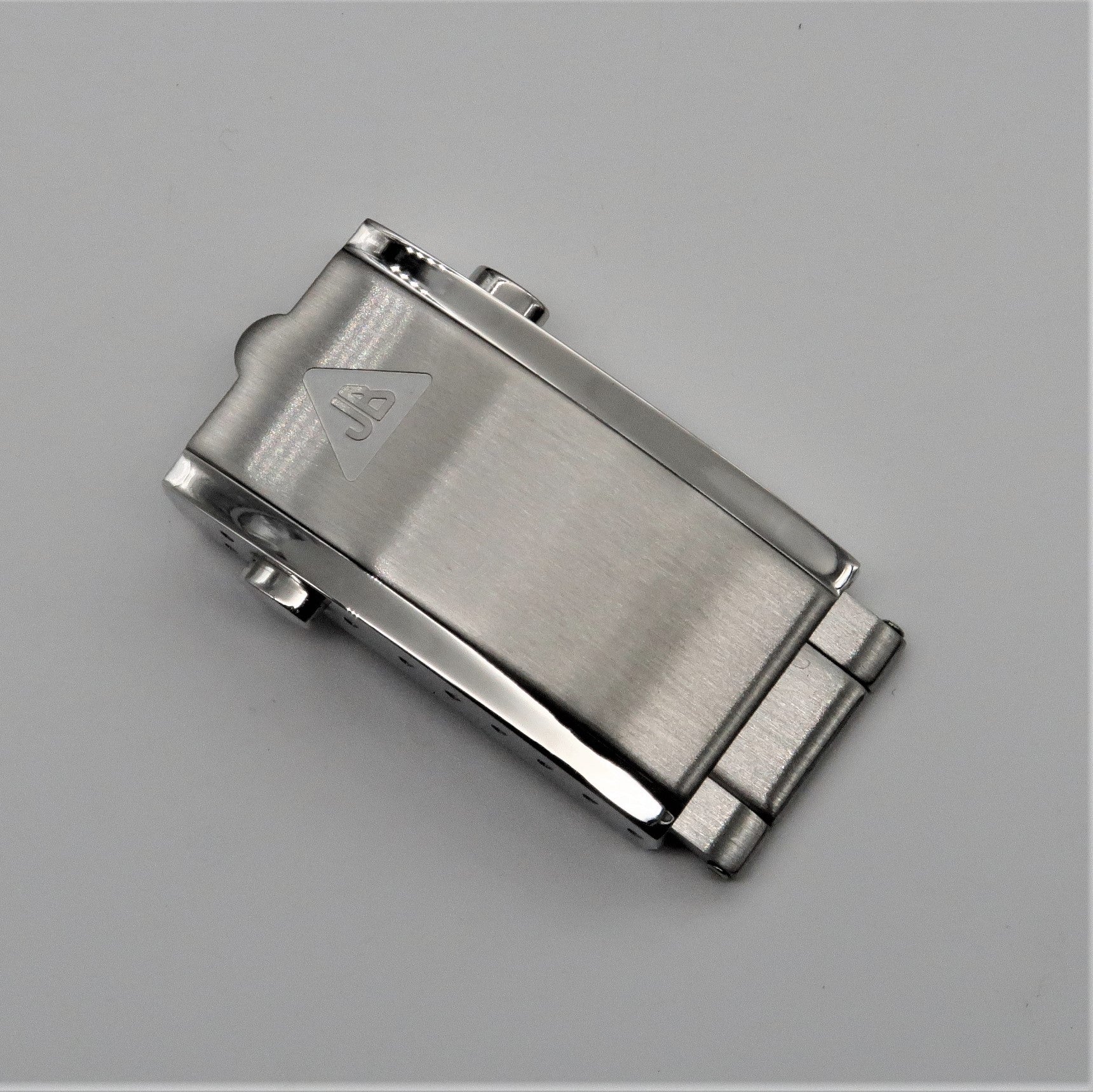 Brushed stainless steel push-button milled clasp with triangular logo and spring mechanism on gray background