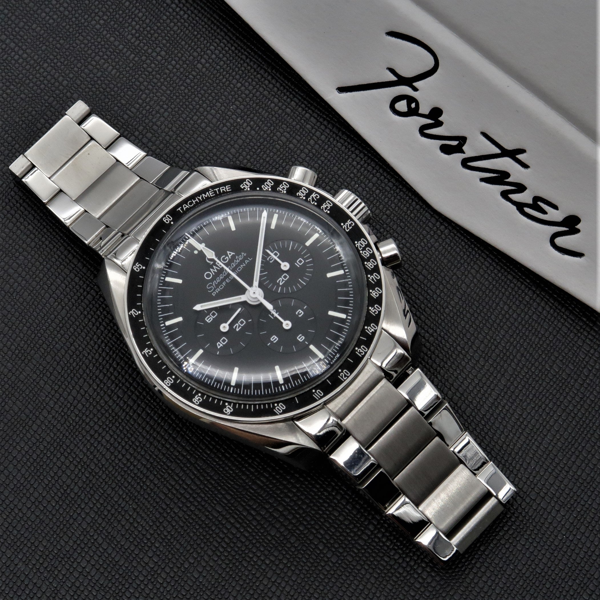 Omega Speedmaster chronograph watch with stainless steel flat link bracelet and black dial on dark textured background