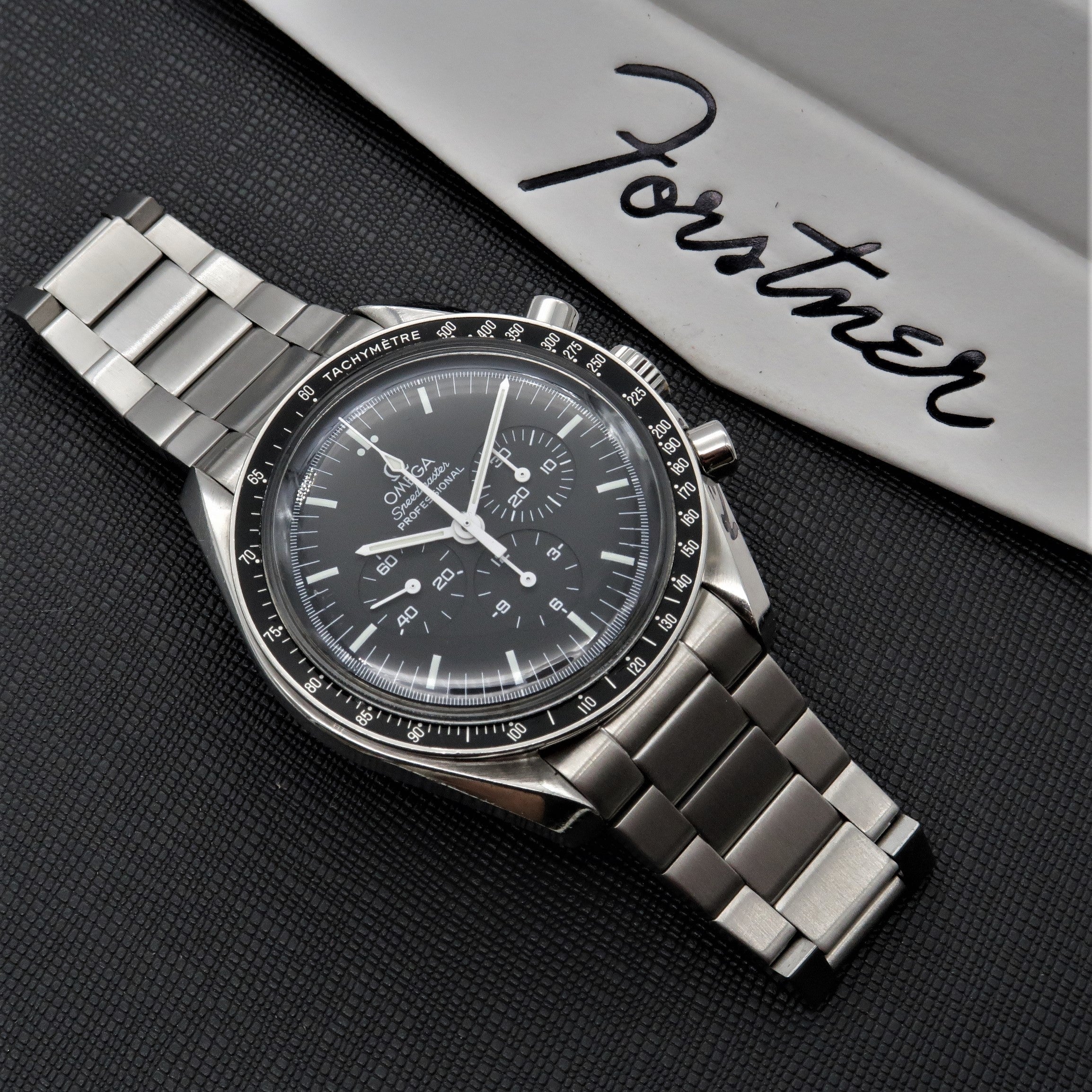 Omega Speedmaster chronograph watch with stainless steel flat link bracelet on black textured background