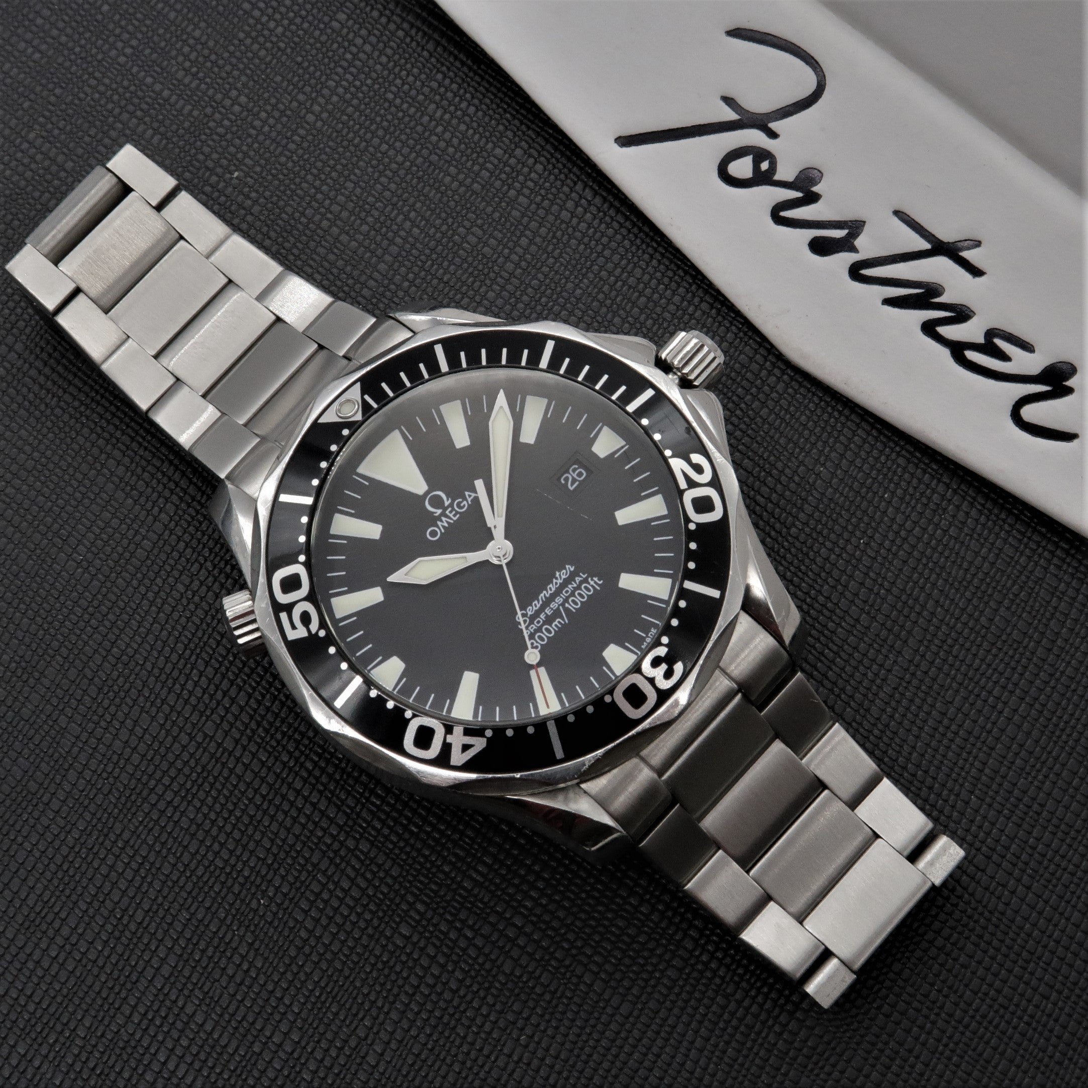 Omega Seamaster dive watch with stainless steel bracelet and black dial on dark textured surface