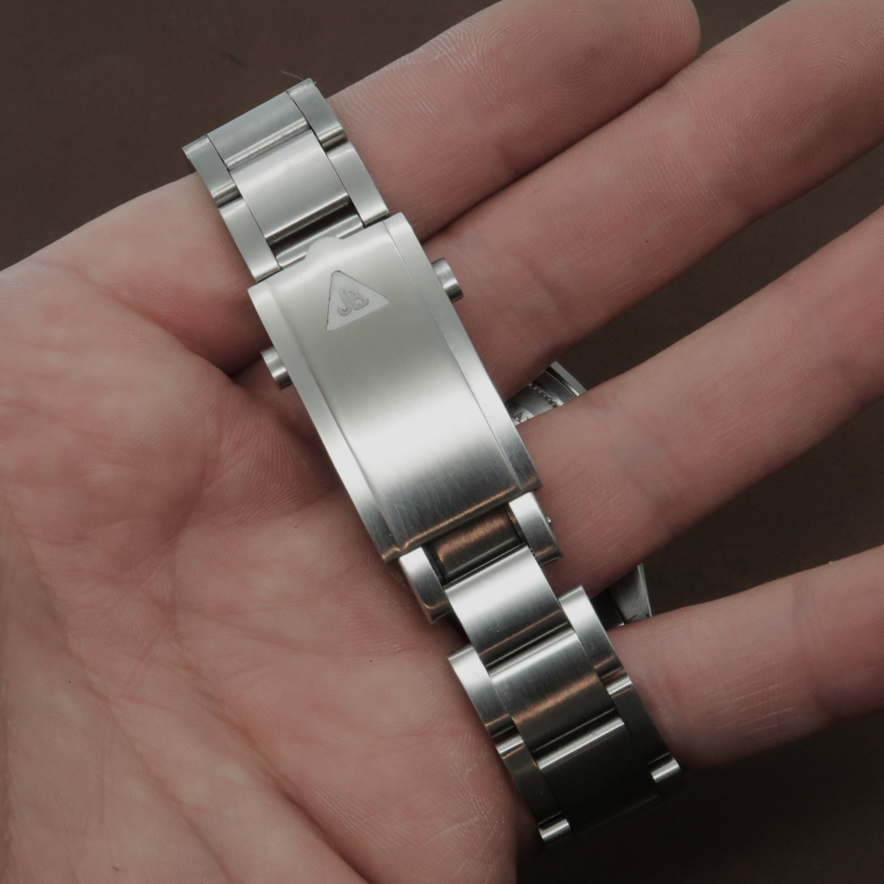 Stainless steel watch bracelet with polished and brushed links held in hand, showing deployment clasp and connector hardware