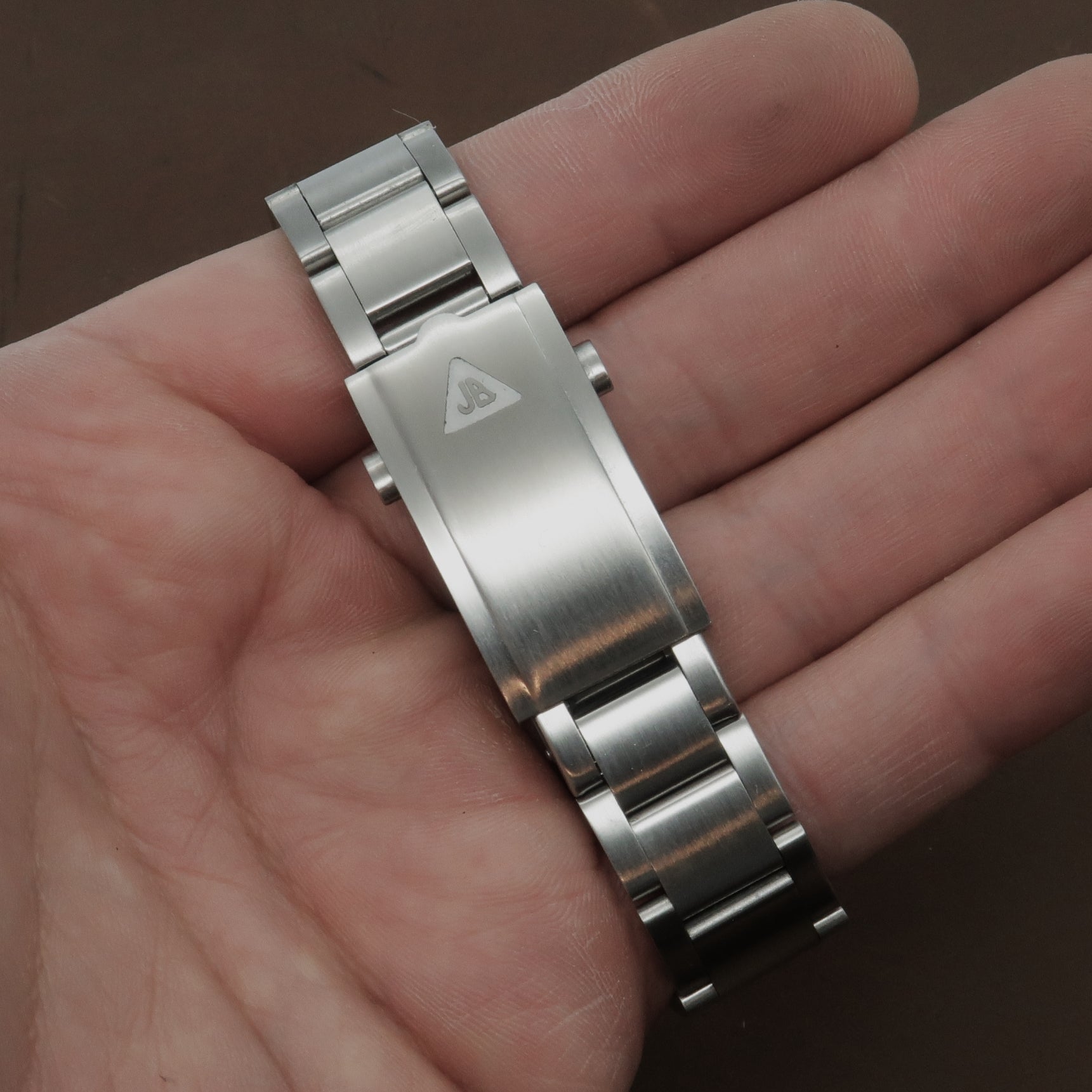 Stainless steel watch bracelet with angular link design held in hand, showing brushed and polished finishing with brand logo