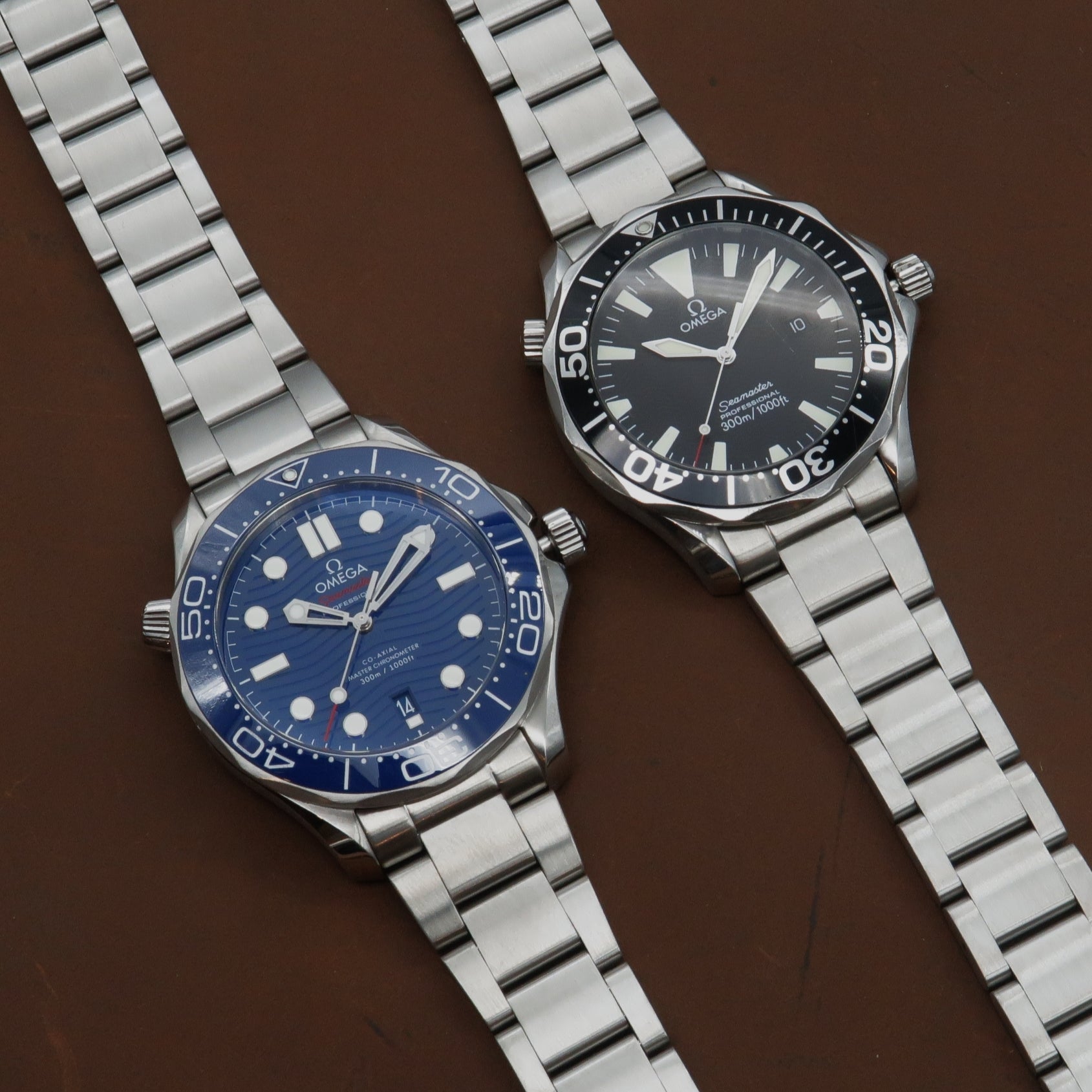 Omega Seamaster diving watches with stainless steel bracelets, blue and black dials, 300m water resistance on brown background
