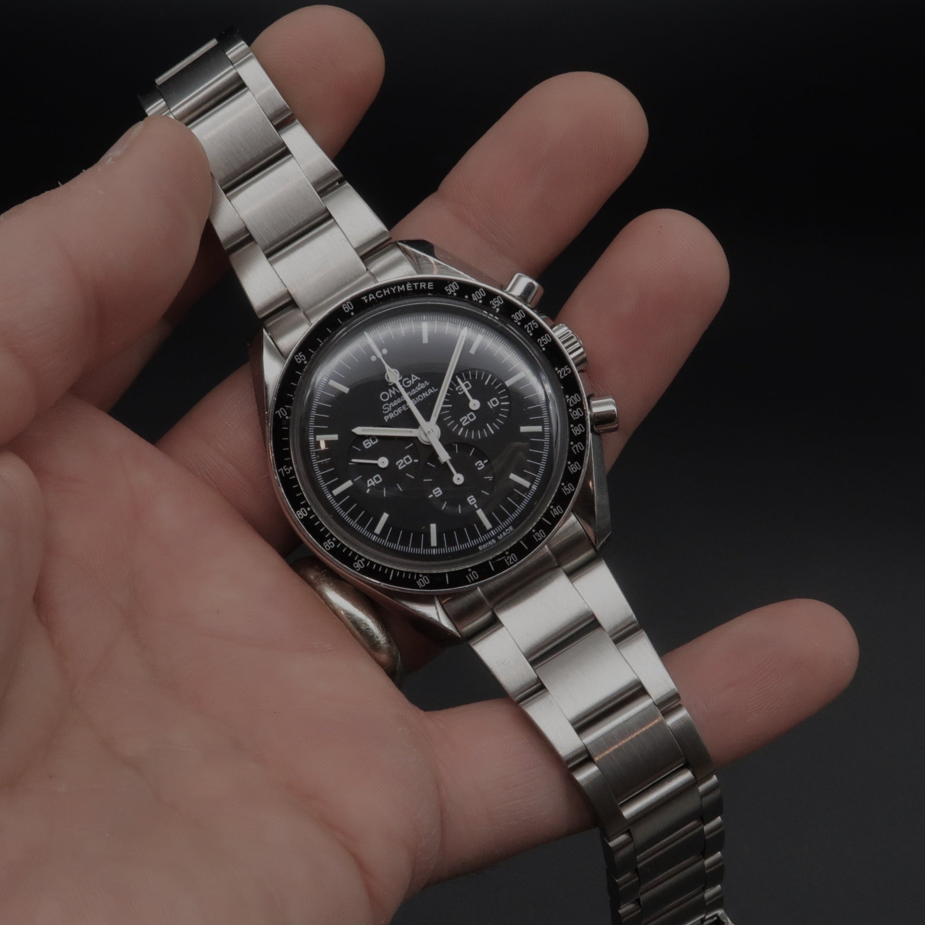 Omega Speedmaster chronograph watch with stainless steel bracelet and black dial held in hand against dark background