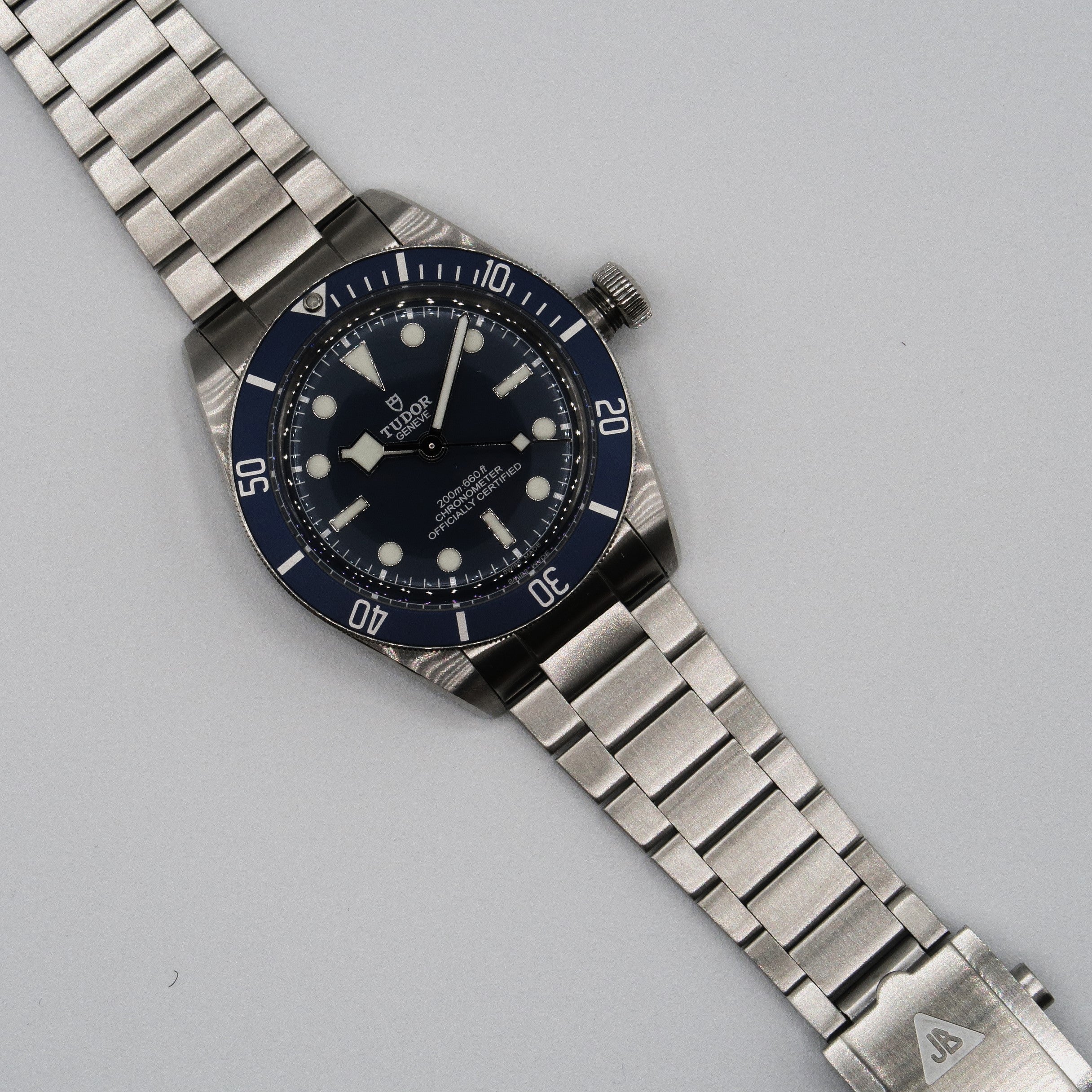 Stainless steel dive watch with black dial, blue bezel, and matching brushed metal bracelet on gray background