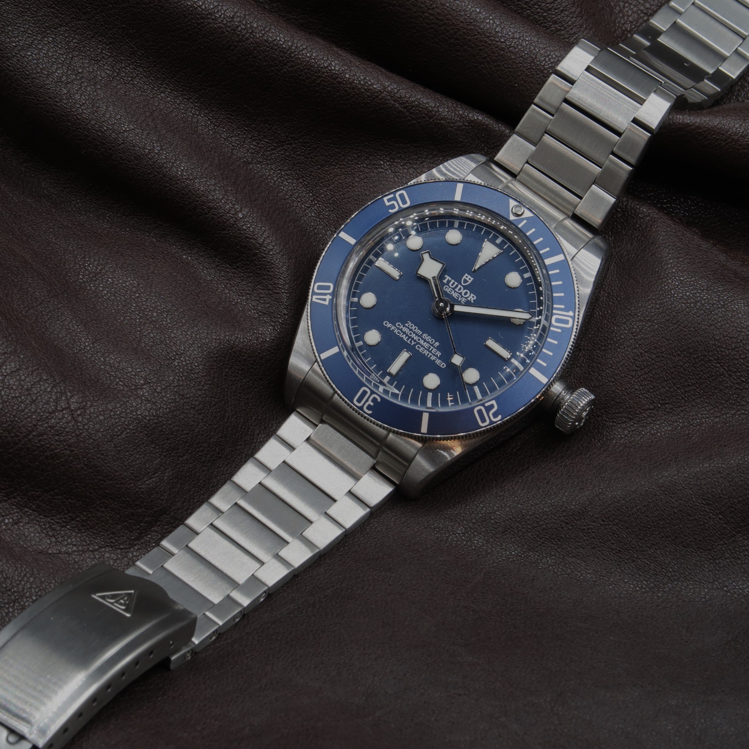 Tudor Black Bay 58 dive watch with blue dial and stainless steel bracelet on black leather background