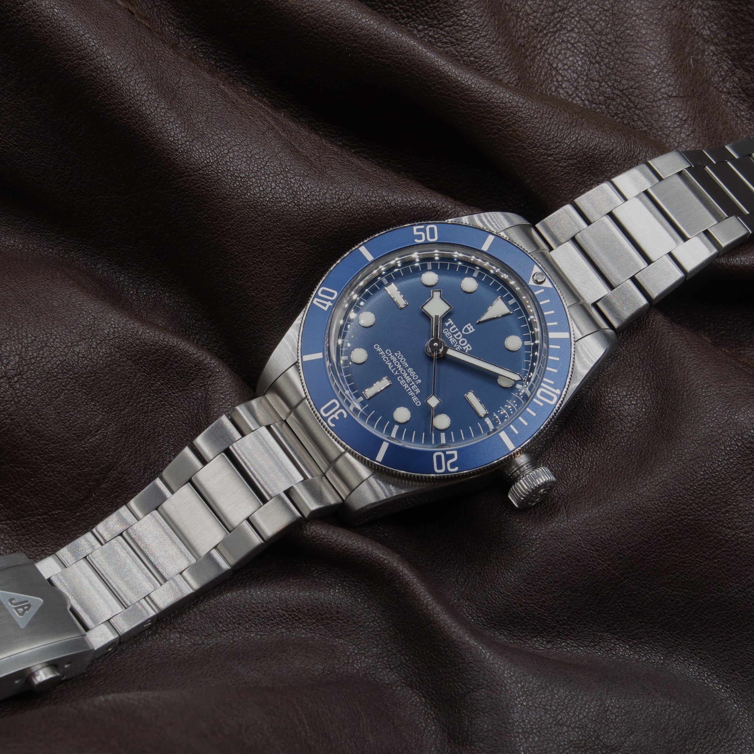 Stainless steel dive watch with blue dial and bezel on brushed metal bracelet against dark leather background