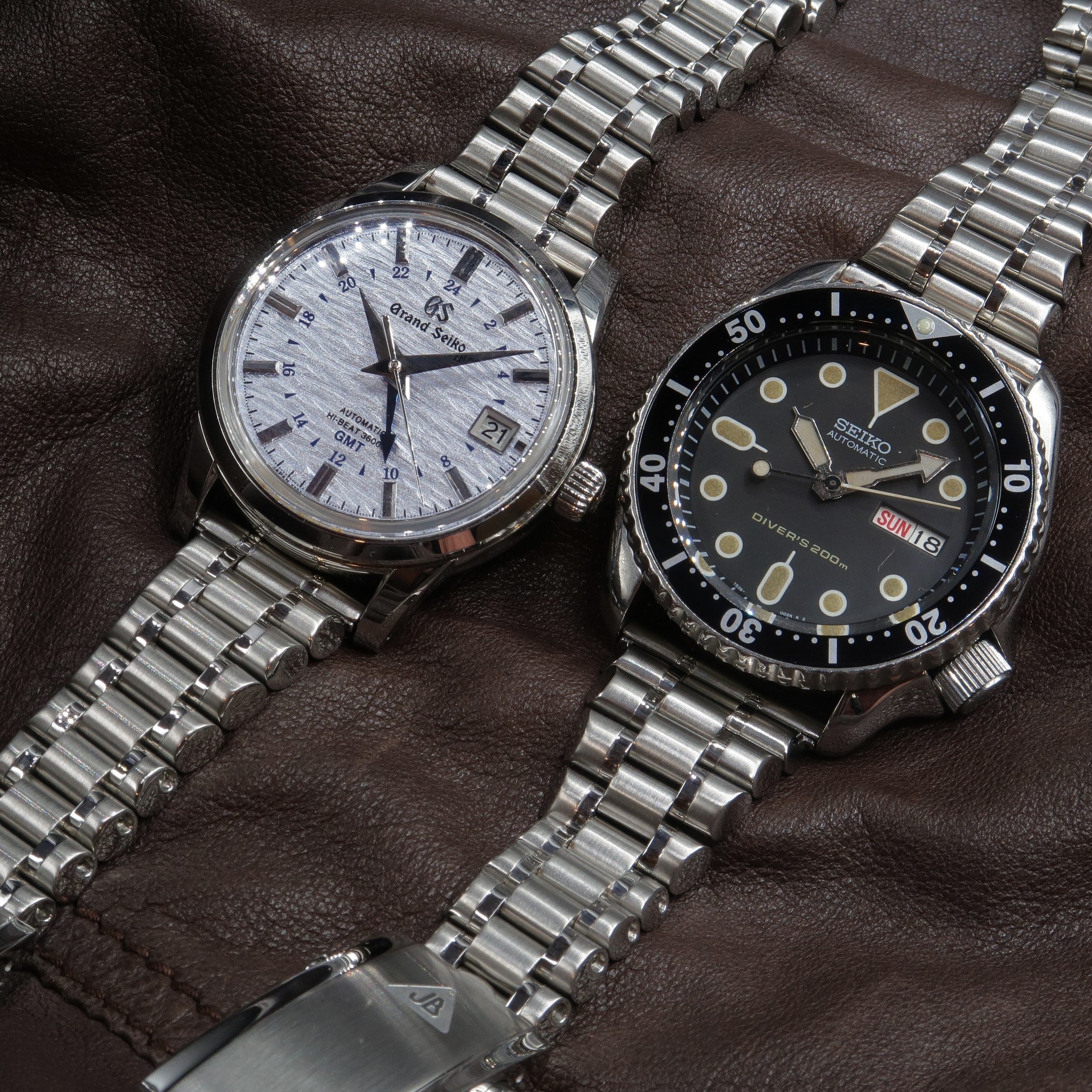 Two Seiko stainless steel watches with metal bracelets on brown leather background
