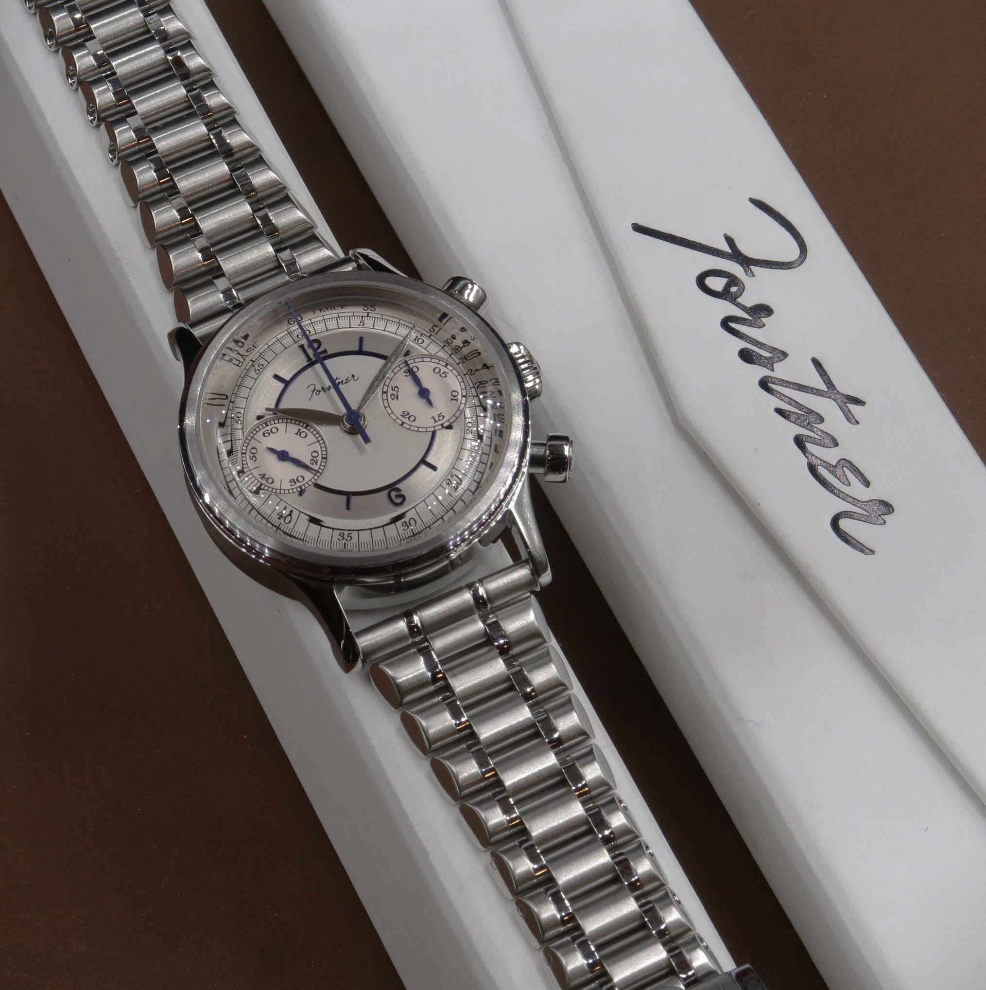 Stainless steel chronograph watch with silver bullet bracelet and cream dial featuring blue hands on white presentation box