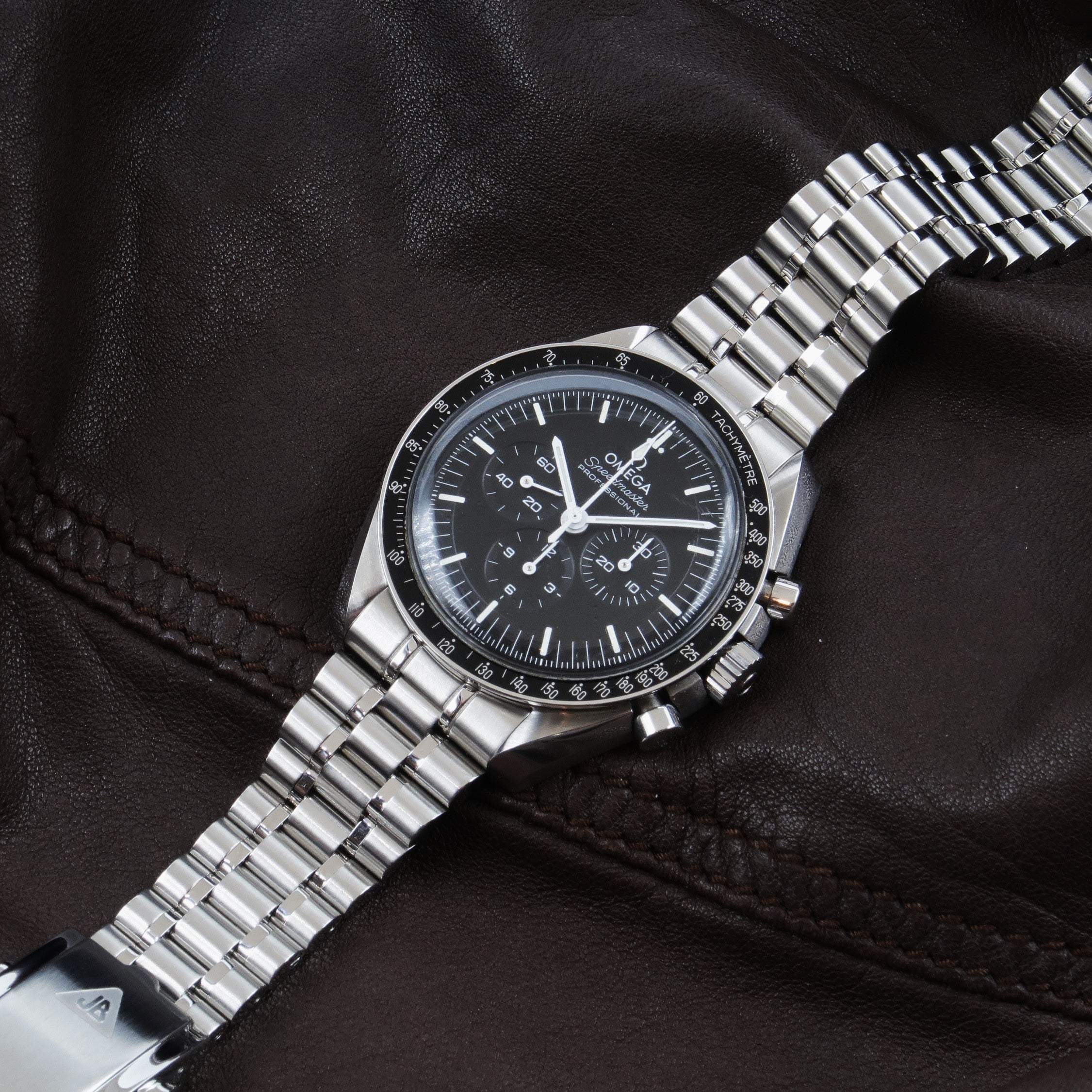 Omega Speedmaster Professional chronograph watch with stainless steel Forstner bullet bracelet on black leather background