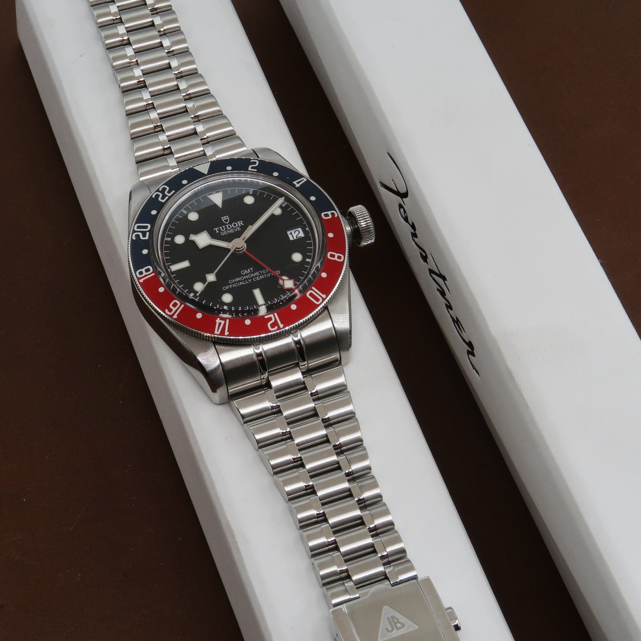 Tudor Black Bay GMT stainless steel watch with red and blue bezel on metal bracelet displayed on white presentation box