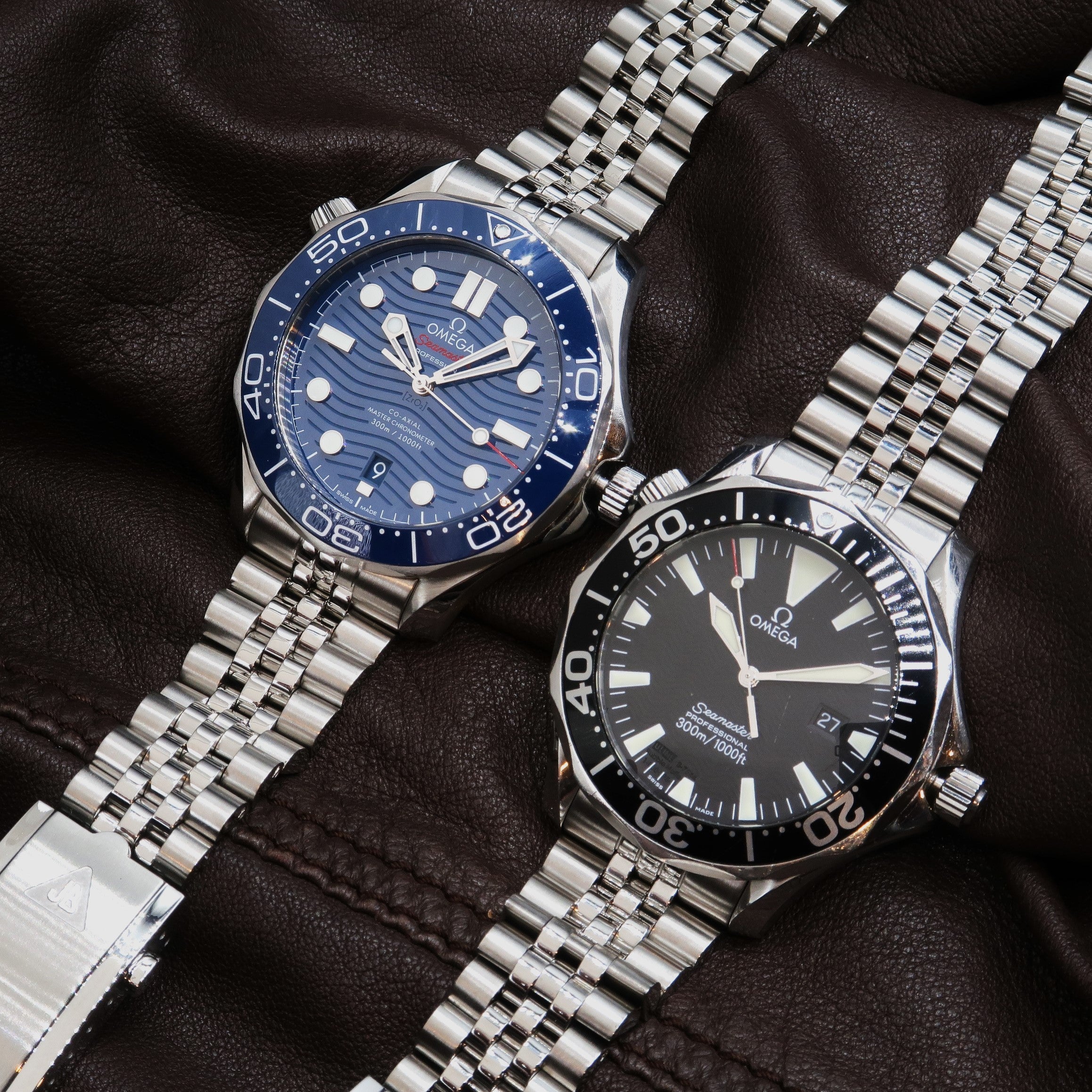Two Omega Seamaster Professional 300M dive watches with stainless steel bracelets on black leather, one with blue dial and one with black dial