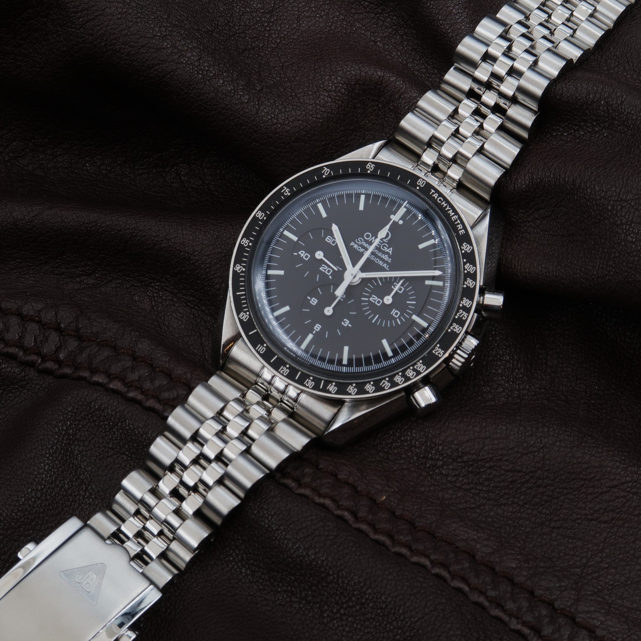 Omega Speedmaster Professional chronograph watch with stainless steel bracelet and black dial on dark fabric background