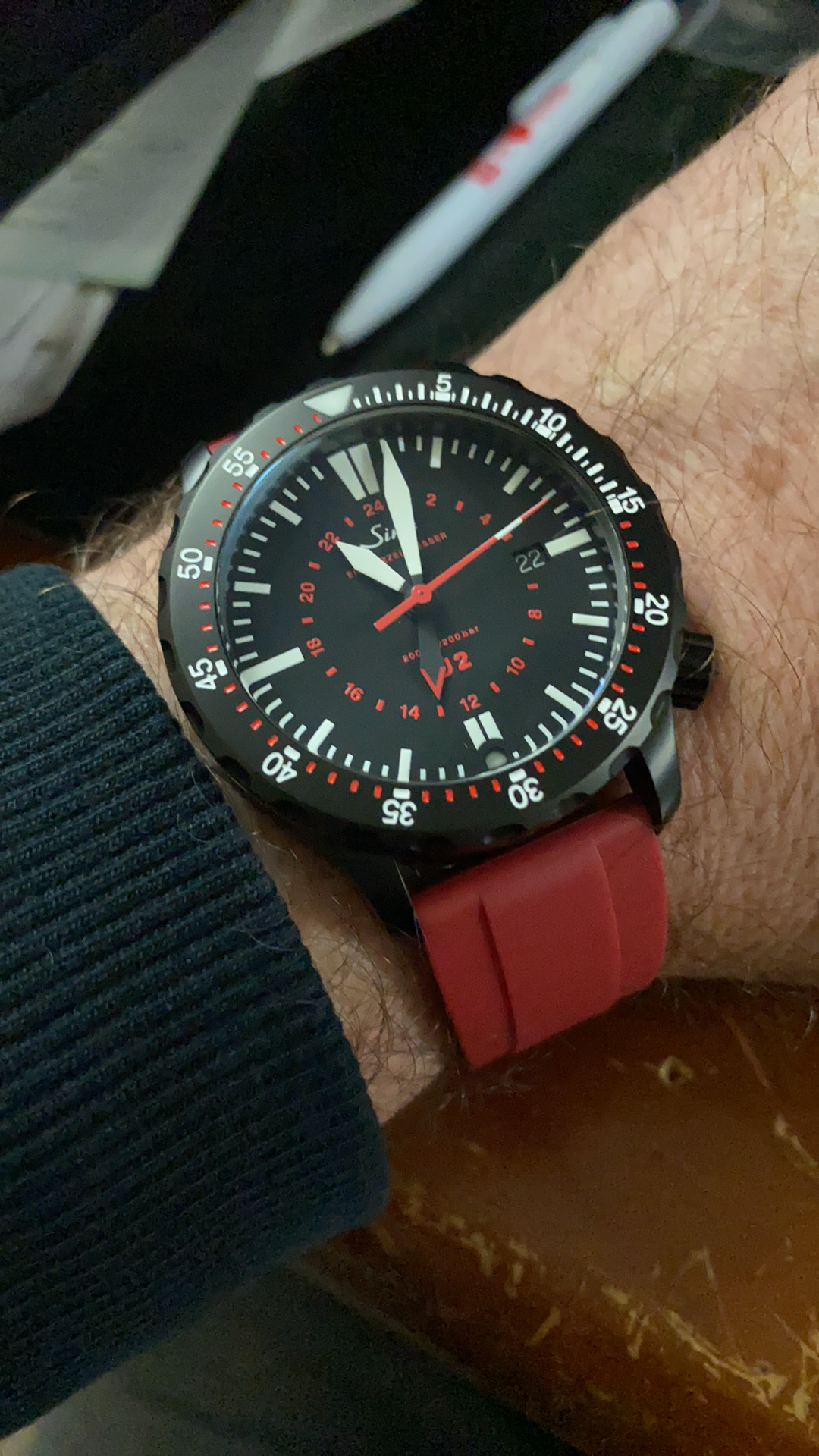 Black dial chronograph watch with red rubber strap and red accents worn on wrist