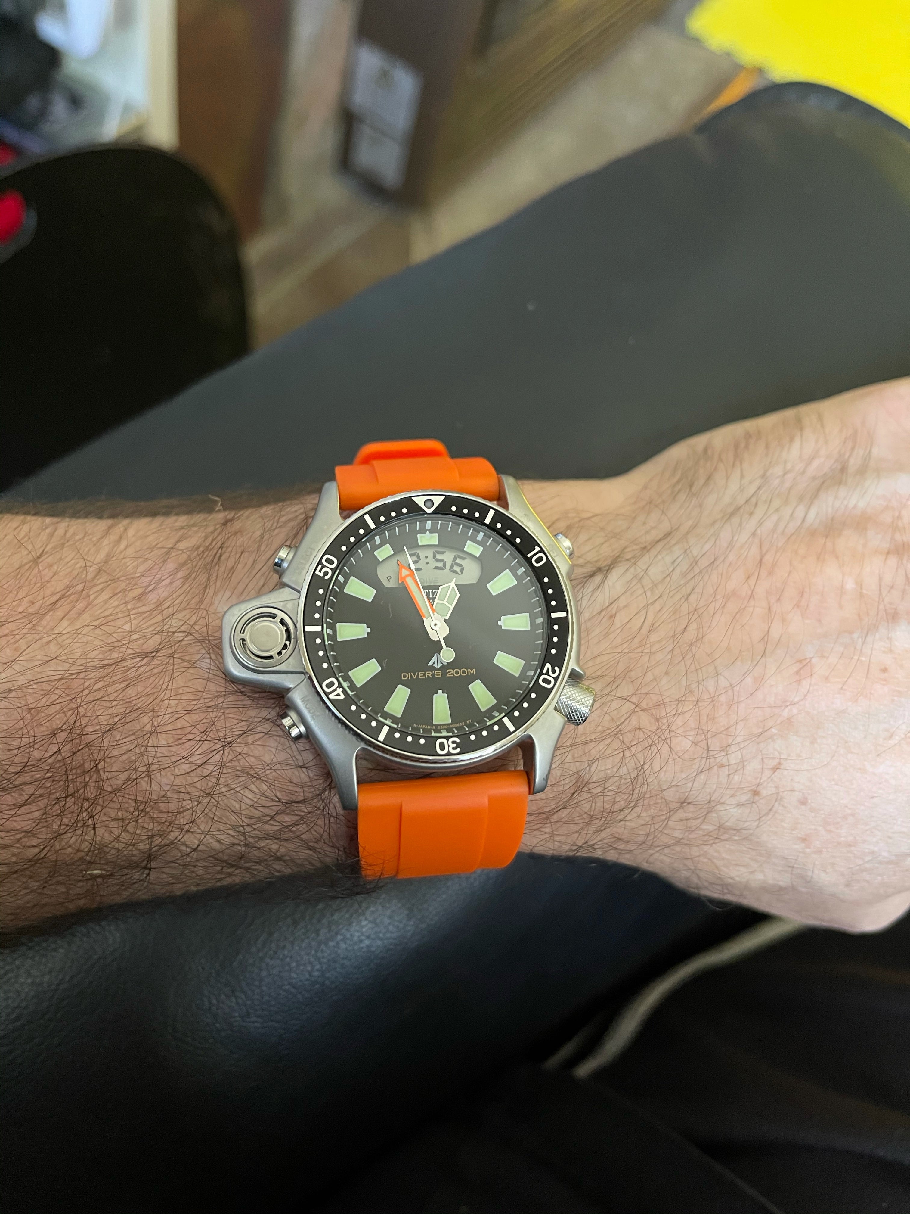 Men's dive watch with orange rubber strap and stainless steel case worn on wrist, featuring black dial and luminous hour markers