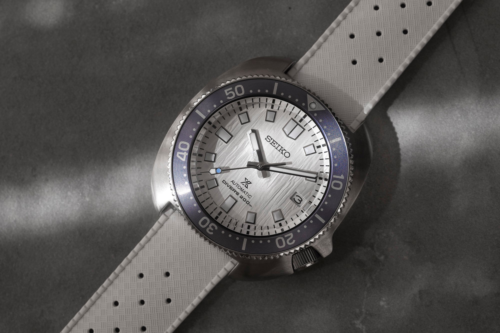 Seiko automatic dive watch with silver dial, black bezel, and white quick-release rubber strap on gray background