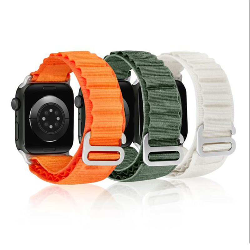 Three Apple Watch Alpine Loop bands in orange, green, and white with adjustable fabric straps and metal buckles