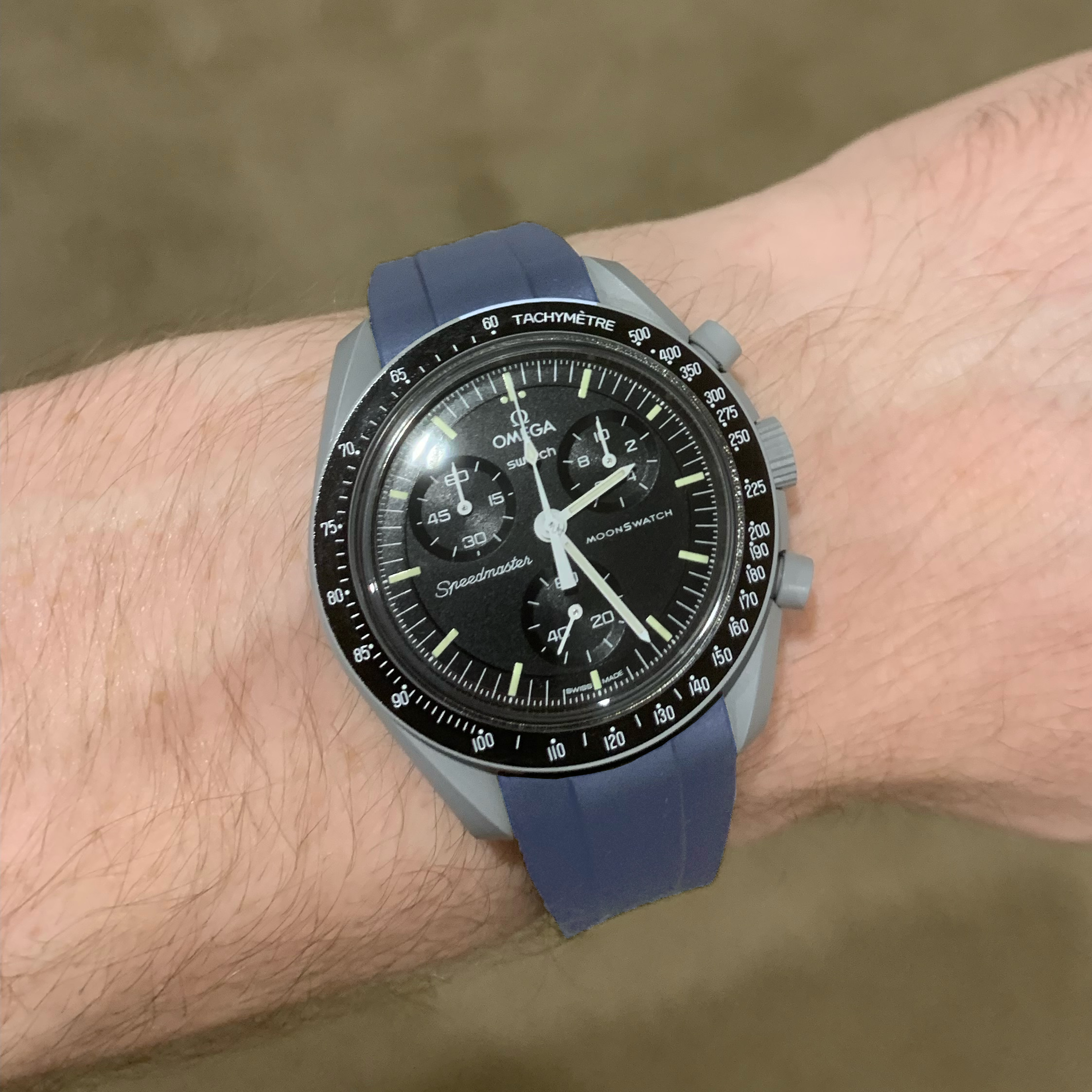 Omega MoonSwatch Speedmaster chronograph watch with black dial, tachymeter bezel, and navy blue rubber strap on wrist