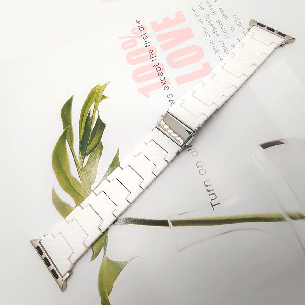 White ceramic Apple Watch band with stainless steel connector, displayed diagonally with green botanical leaves on white background
