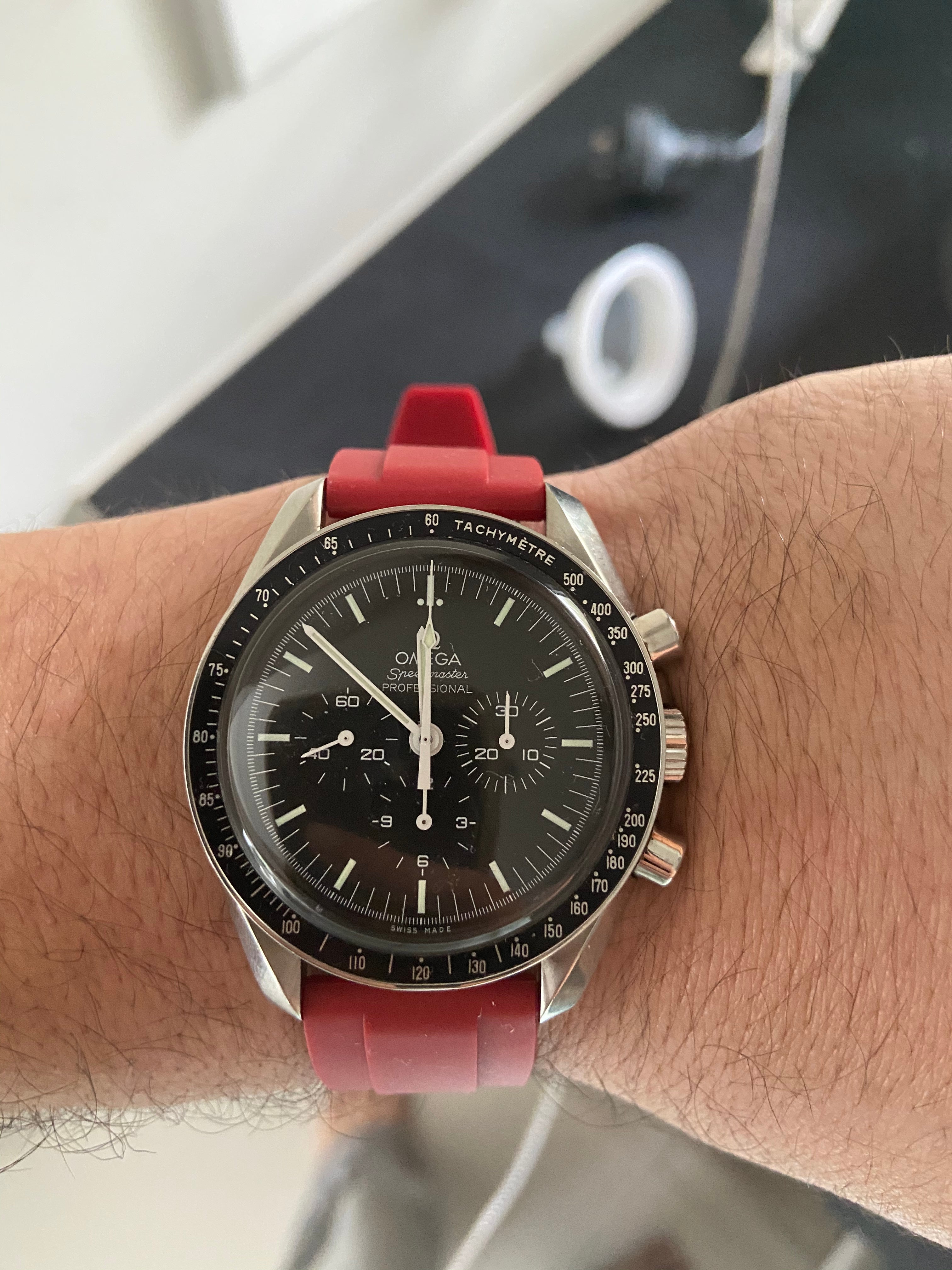 Omega Speedmaster Professional chronograph watch with black dial and red rubber quick release strap on wrist
