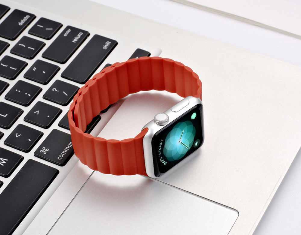 Smartwatch with red magnetic silicone loop band on laptop keyboard, displaying time on turquoise watch face