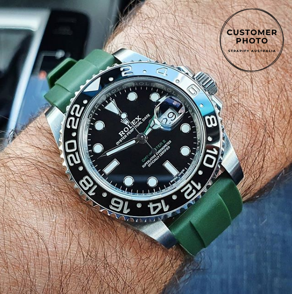 Luxury sports watch with black dial and GMT bezel on forest green quick release rubber strap worn on wrist
