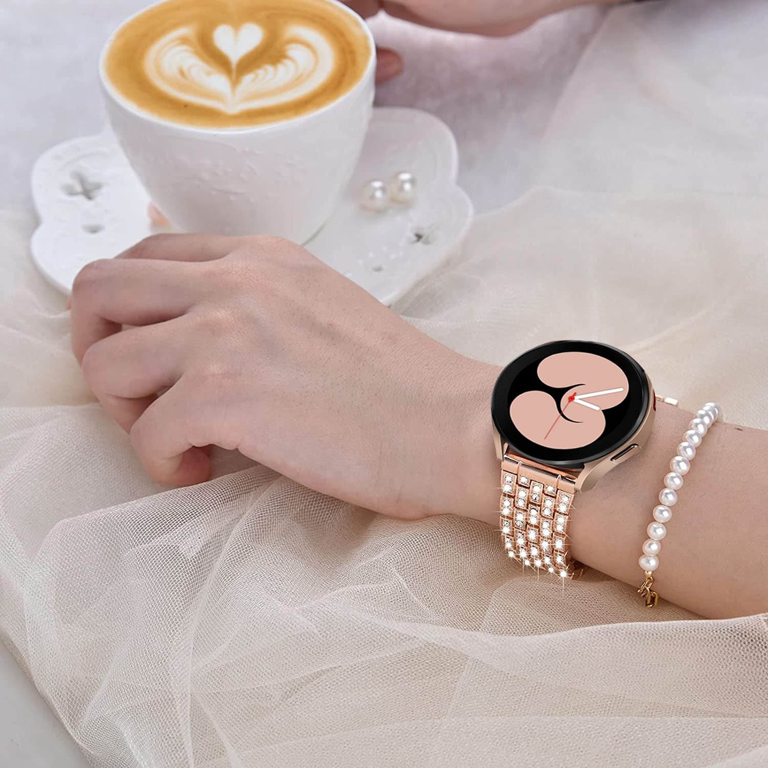 Woman wearing rose gold smartwatch with shimmer bracelet and pearl bracelet while holding latte with latte art