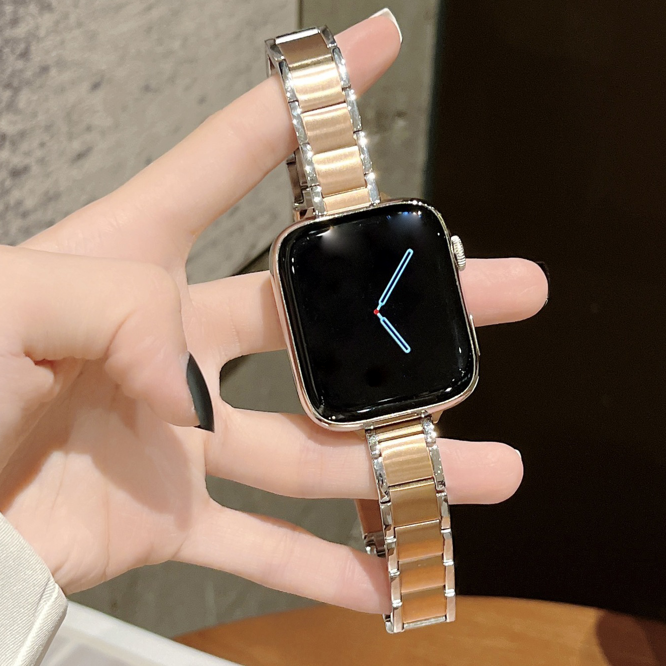 Rose gold and crystal link smartwatch band on square faced watch with black display held in hand