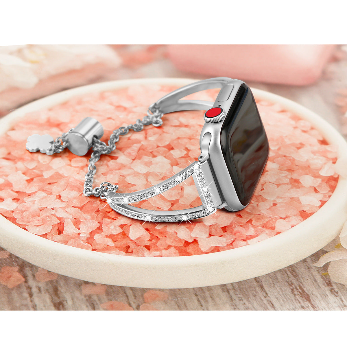 Silver smartwatch band with crystal-studded cuff and red accent button on pink rose petal background
