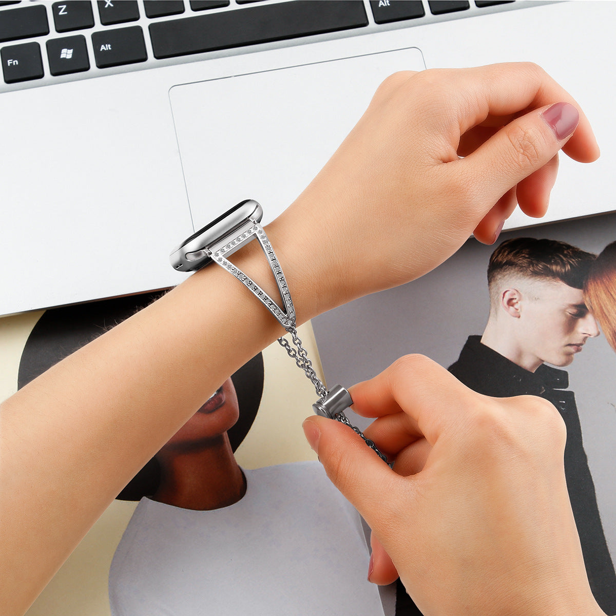Woman wearing silver diamond-studded Apple Watch band bracelet at desk with keyboard and laptop