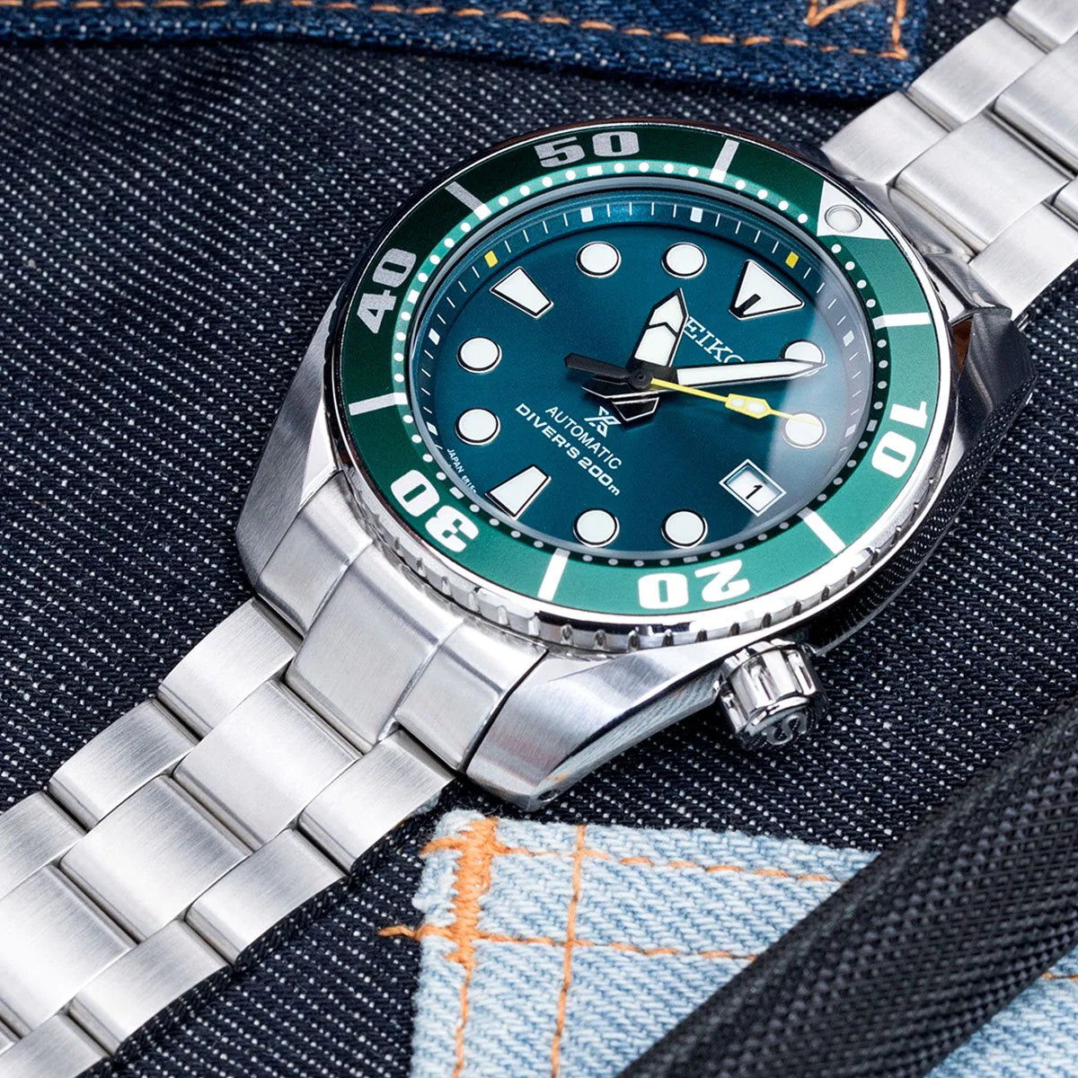 Stainless steel dive watch with teal bezel and dial on matching Super-O Boyer bracelet, displayed on denim background