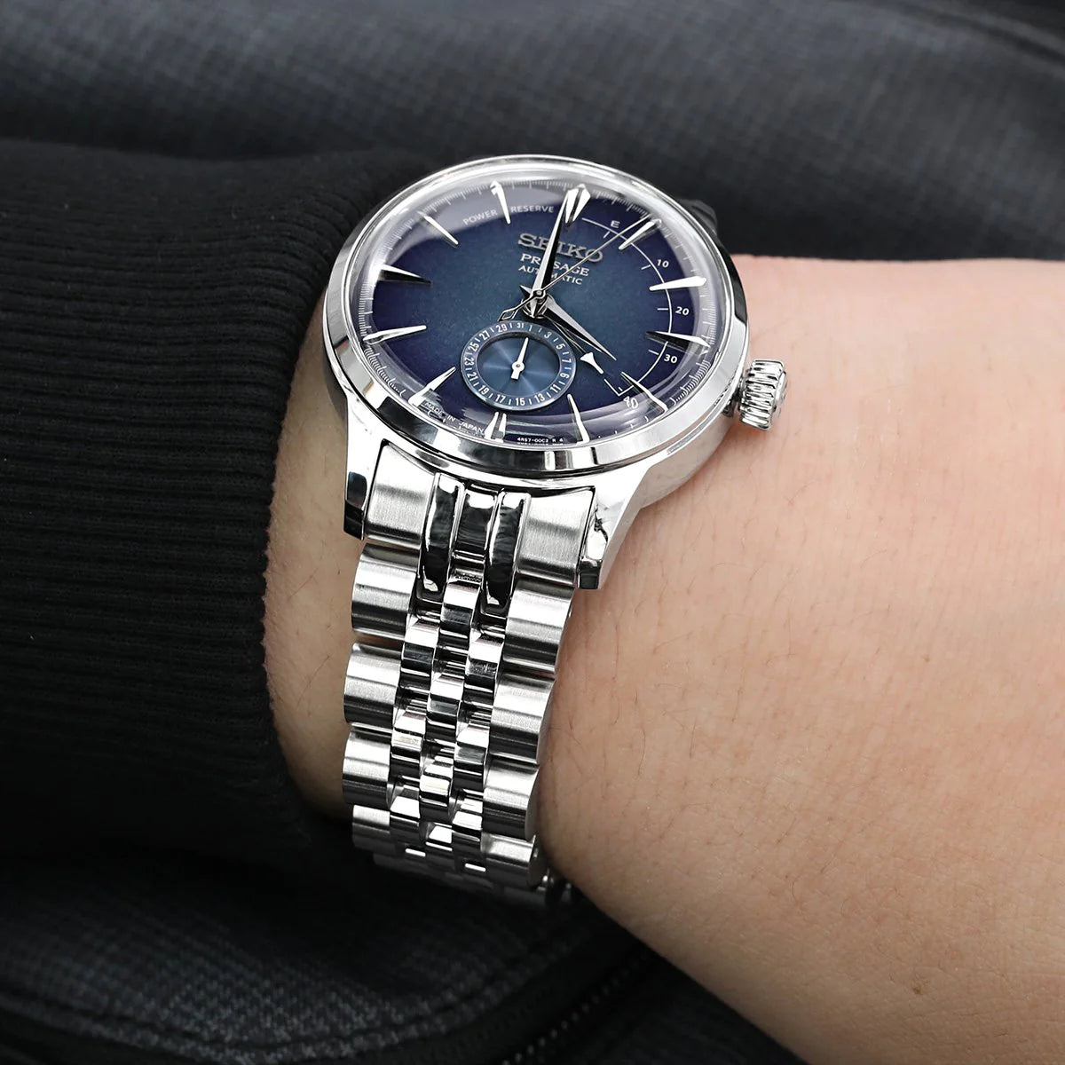 Silver stainless steel bracelet watch with dark blue dial, moon phase subdial, and jubilee-style metal band worn on wrist
