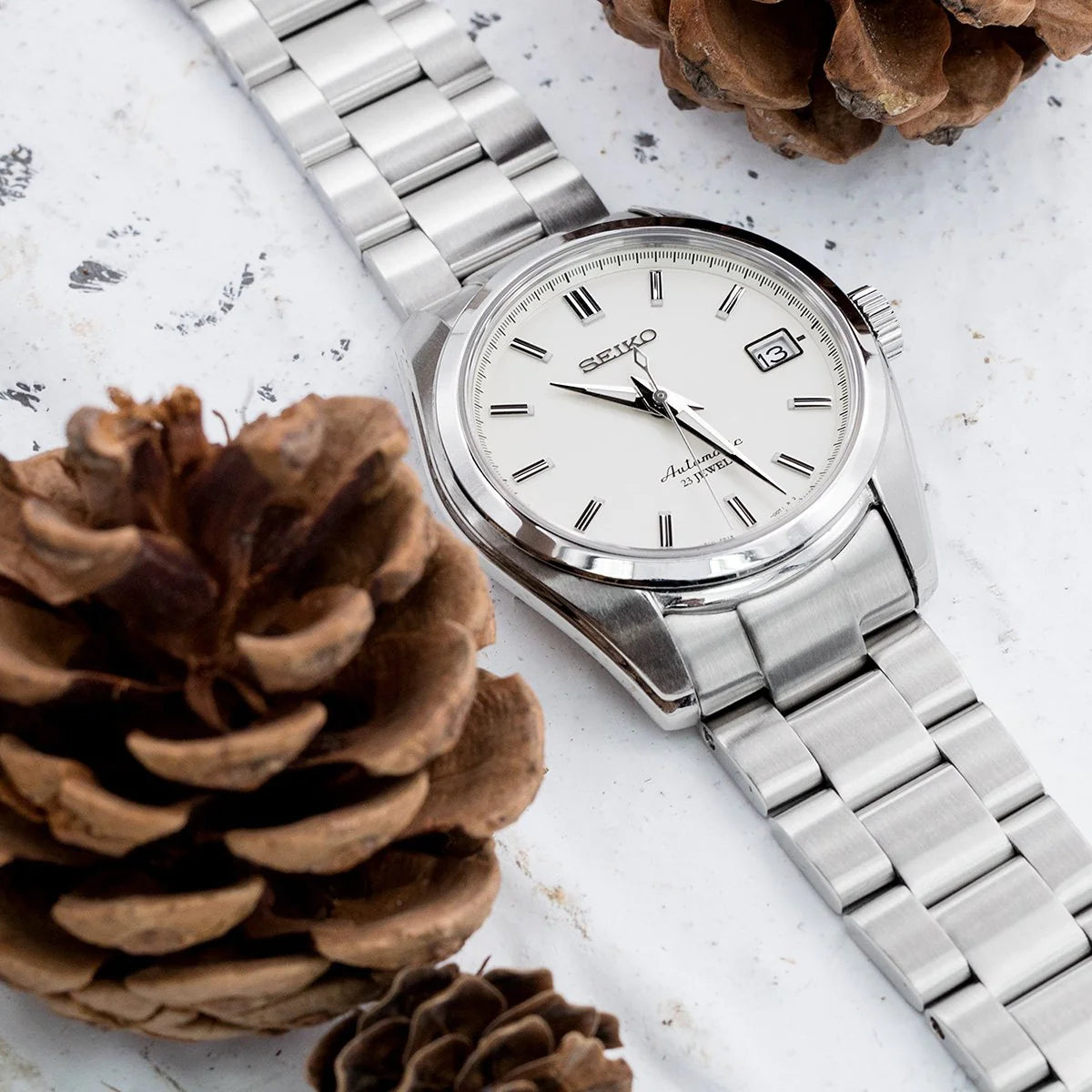 Seiko SARB035 watch with stainless steel Super-O Boyer bracelet on white marble surface with pinecones