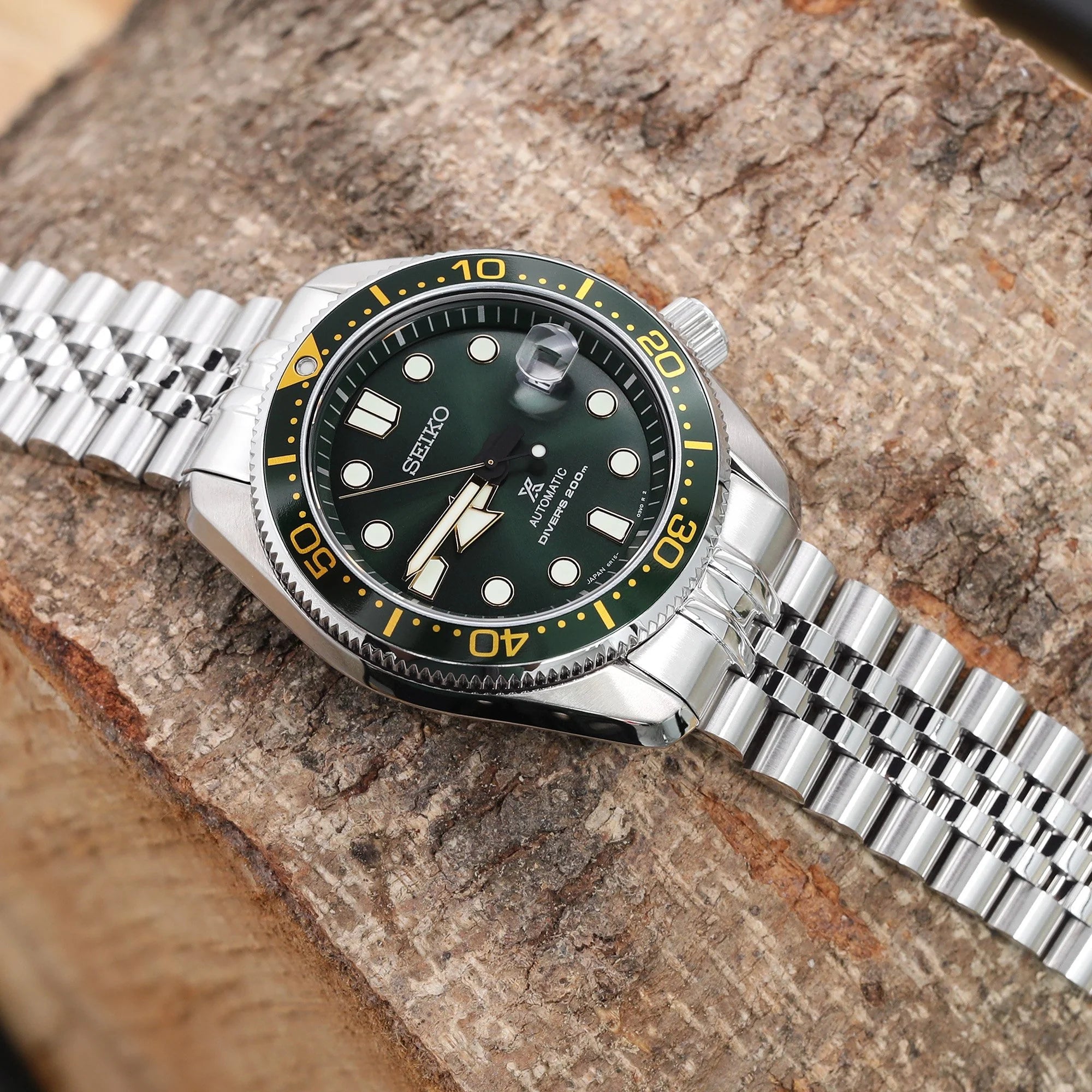 Seiko Baby MarineMaster MM200 dive watch with Super-J Jub stainless steel bracelet, black dial, yellow bezel, on textured stone background