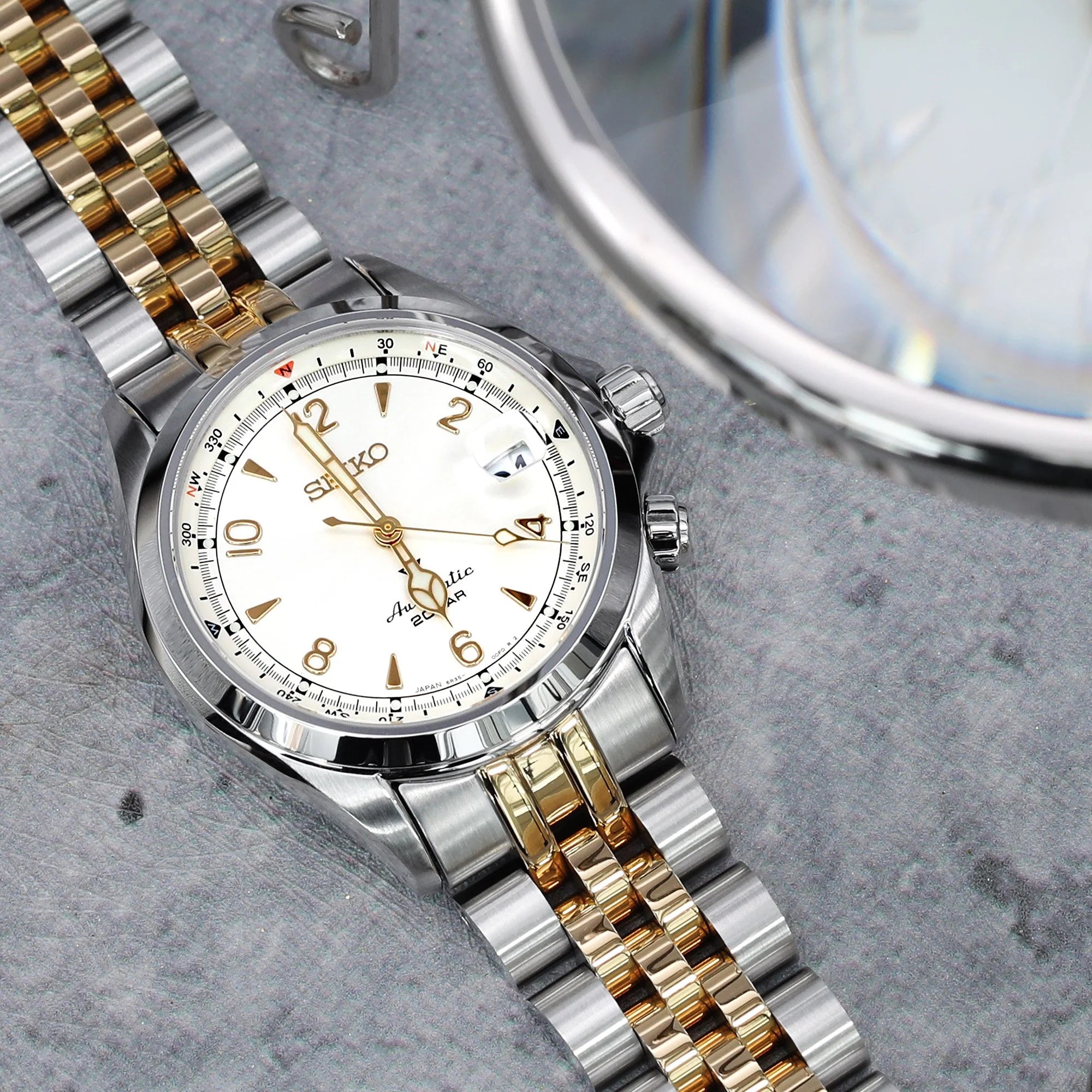 Two-tone stainless steel watch bracelet with silver and gold links displayed on gray surface next to watch case