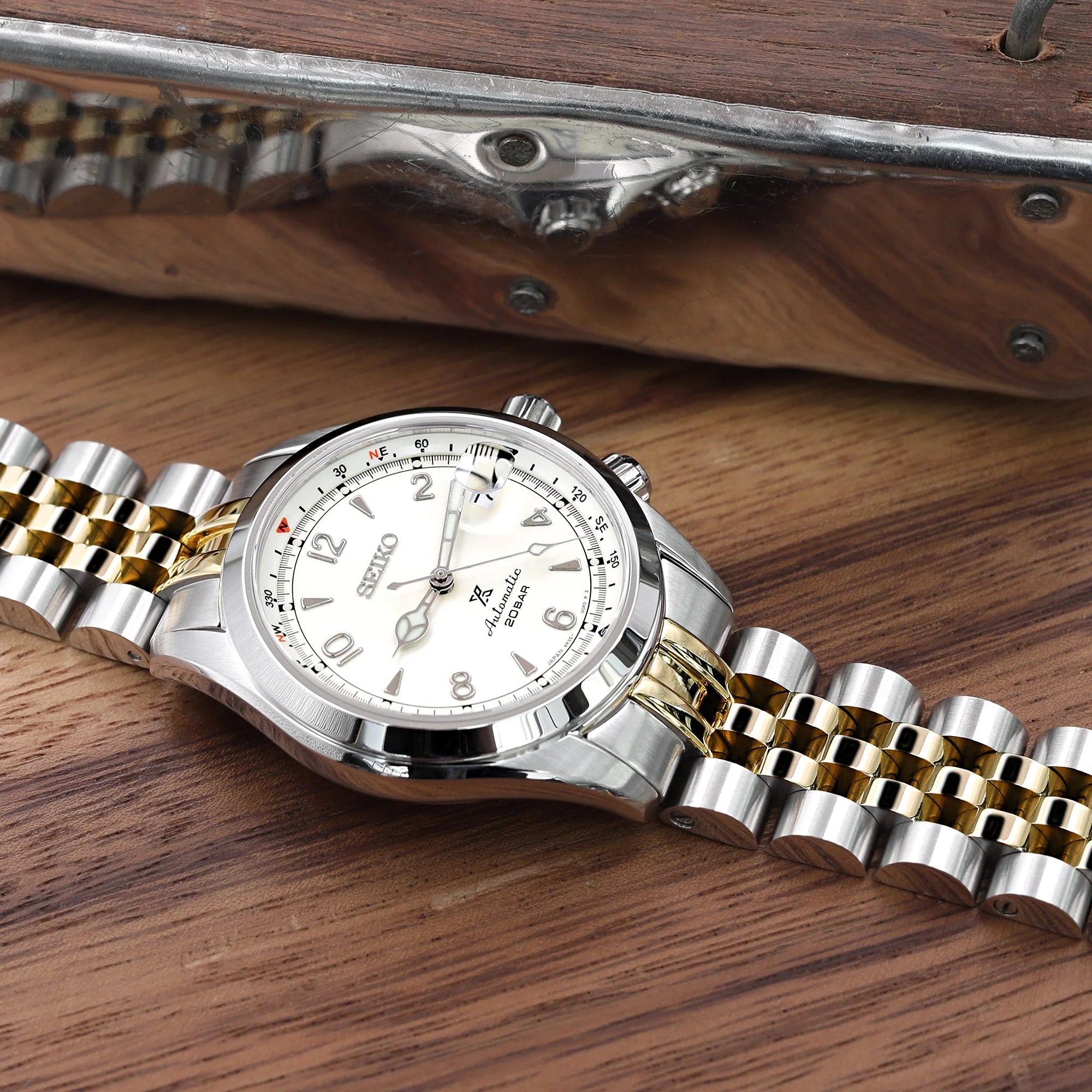 Seiko Alpinist SARB017 two-tone stainless steel watch with jubilee bracelet on wooden surface next to rifle