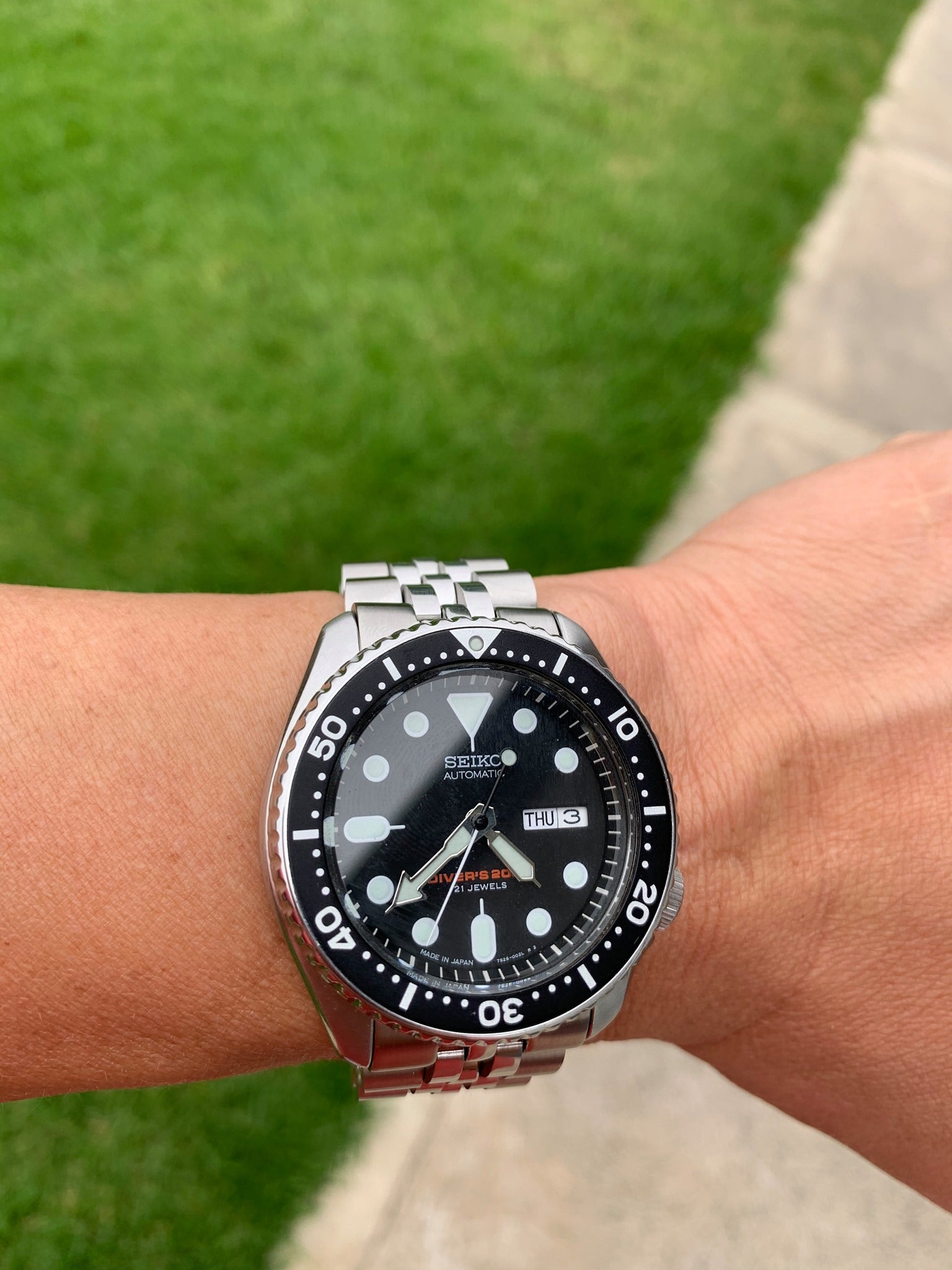 Seiko automatic dive watch with black dial and stainless steel jubilee bracelet on wrist outdoors