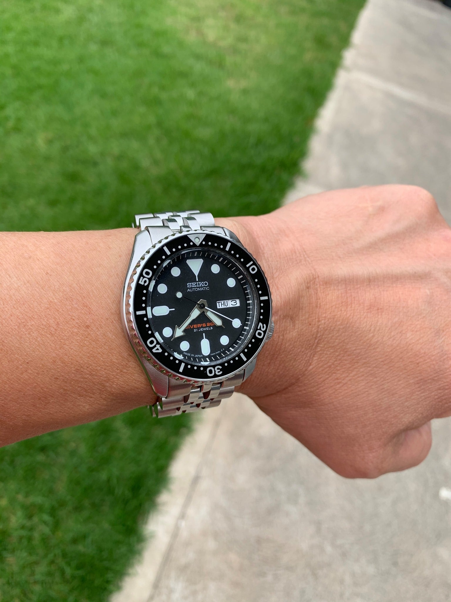 Seiko automatic dive watch with black dial and stainless steel Jubilee bracelet worn on wrist outdoors