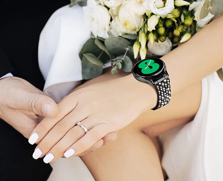 Black smartwatch with diamond-encrusted band and green watch face on woman's wrist with white nail polish