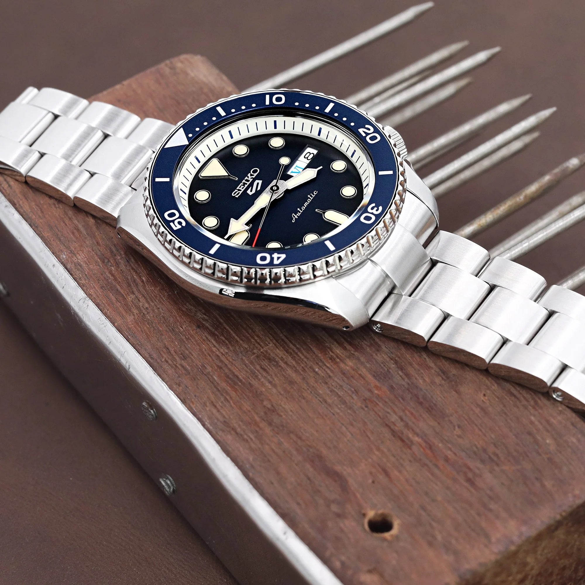 Seiko 5 sports watch with stainless steel Super-O Boyer bracelet and blue bezel on wooden display stand