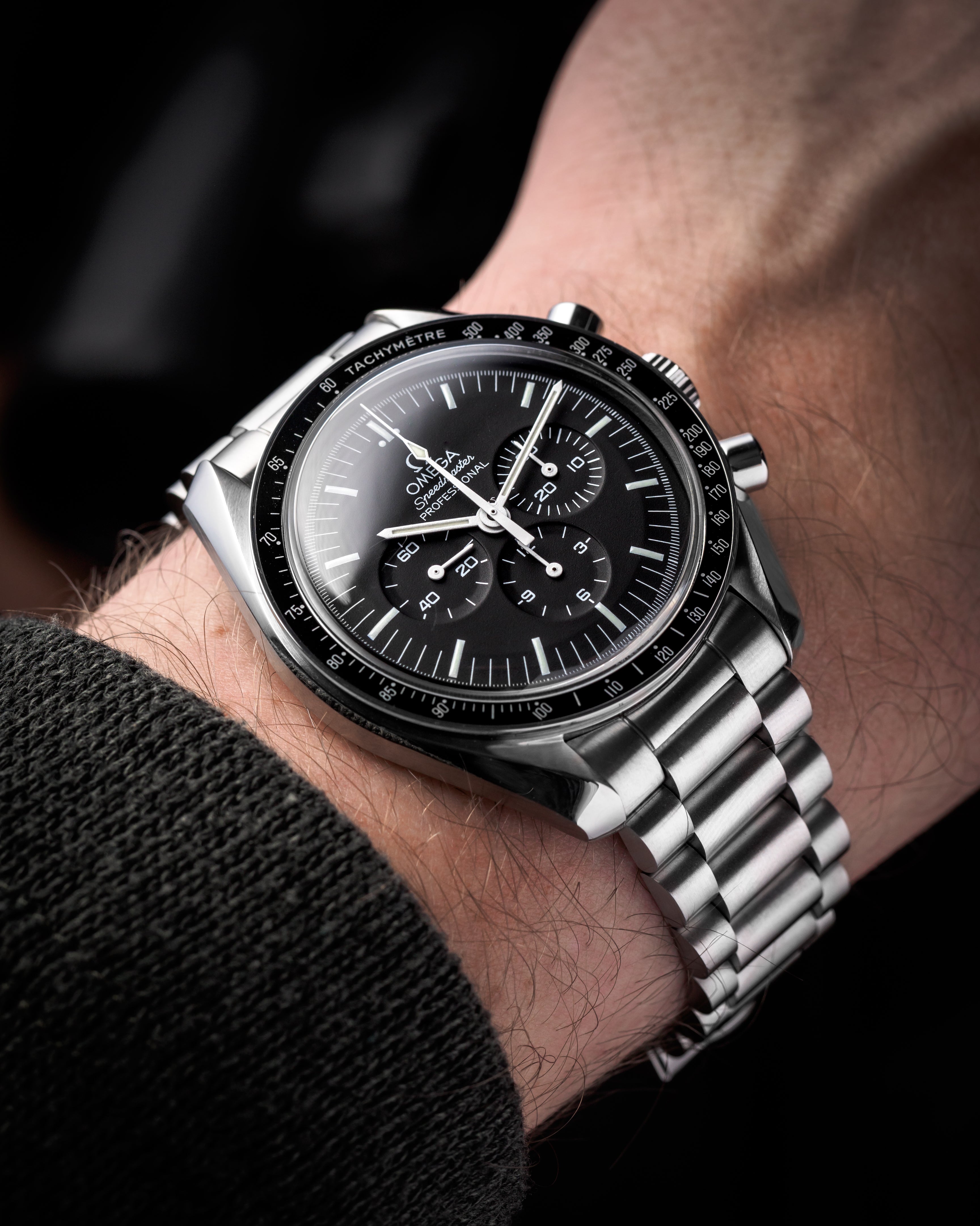 Omega Speedmaster chronograph watch with stainless steel bracelet worn on wrist, black dial with tachymetre bezel