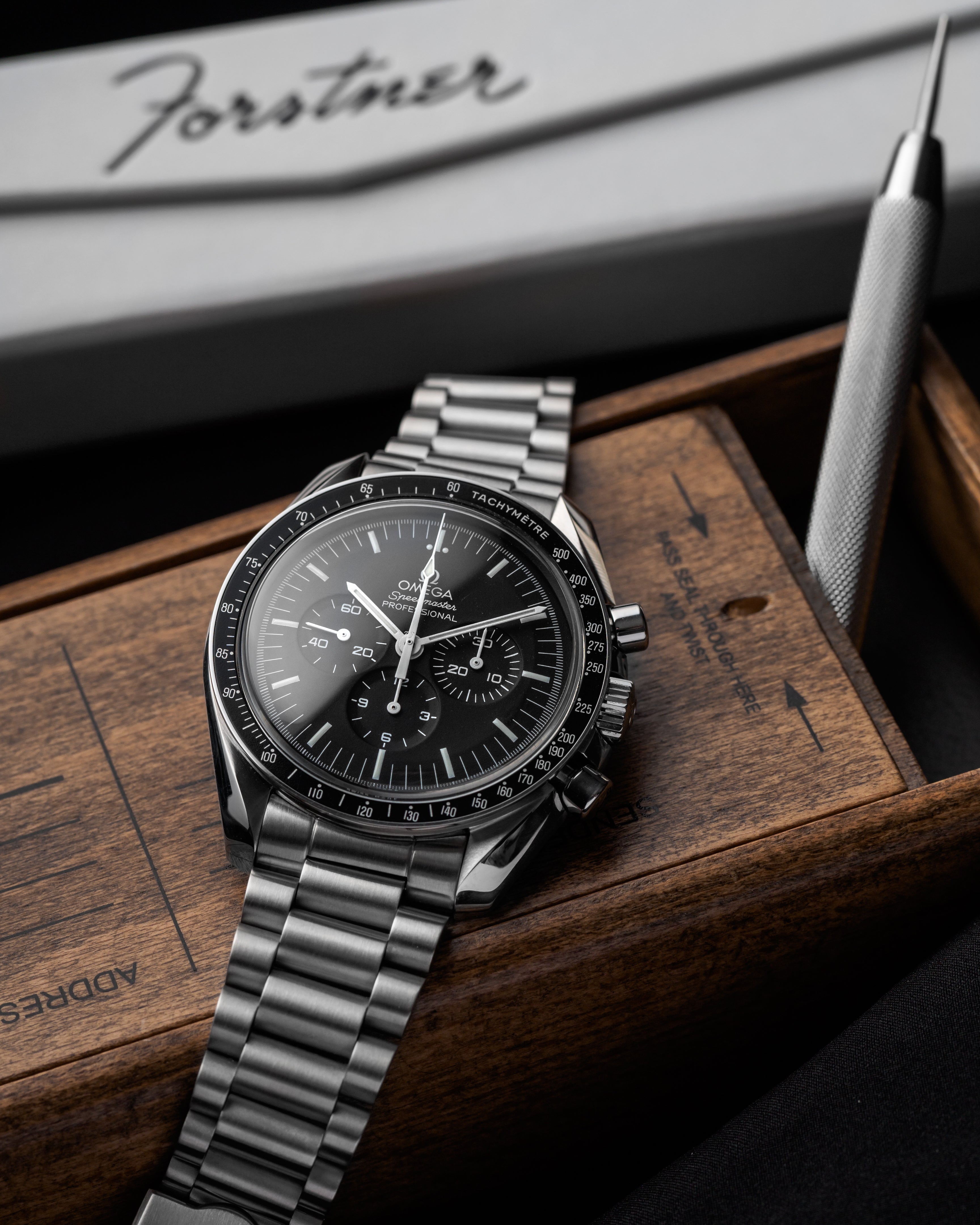 Omega Speedmaster chronograph watch with stainless steel bracelet on wooden display box with pen