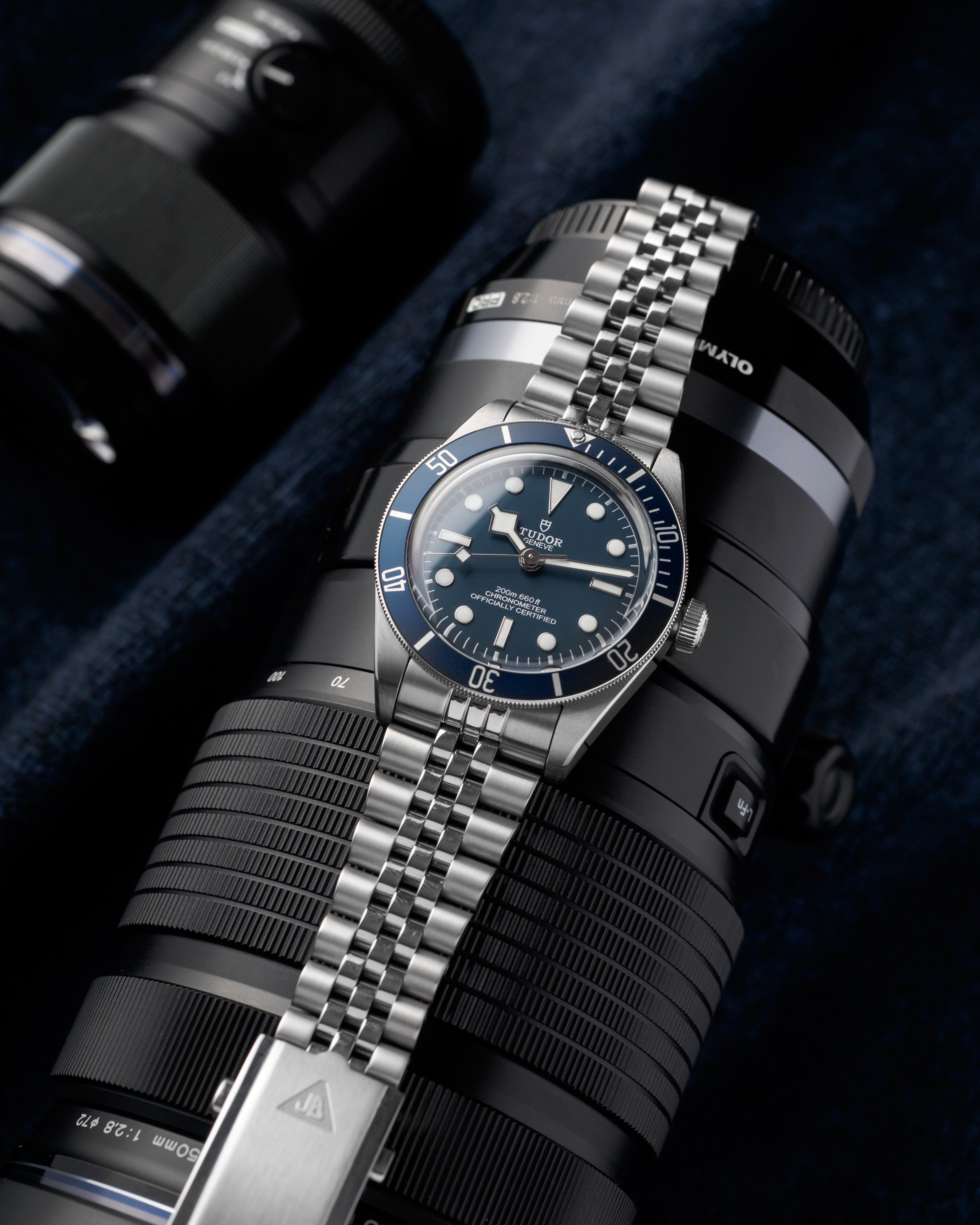 Tudor Black Bay dive watch with stainless steel jubilee bracelet and blue dial on camera lens background