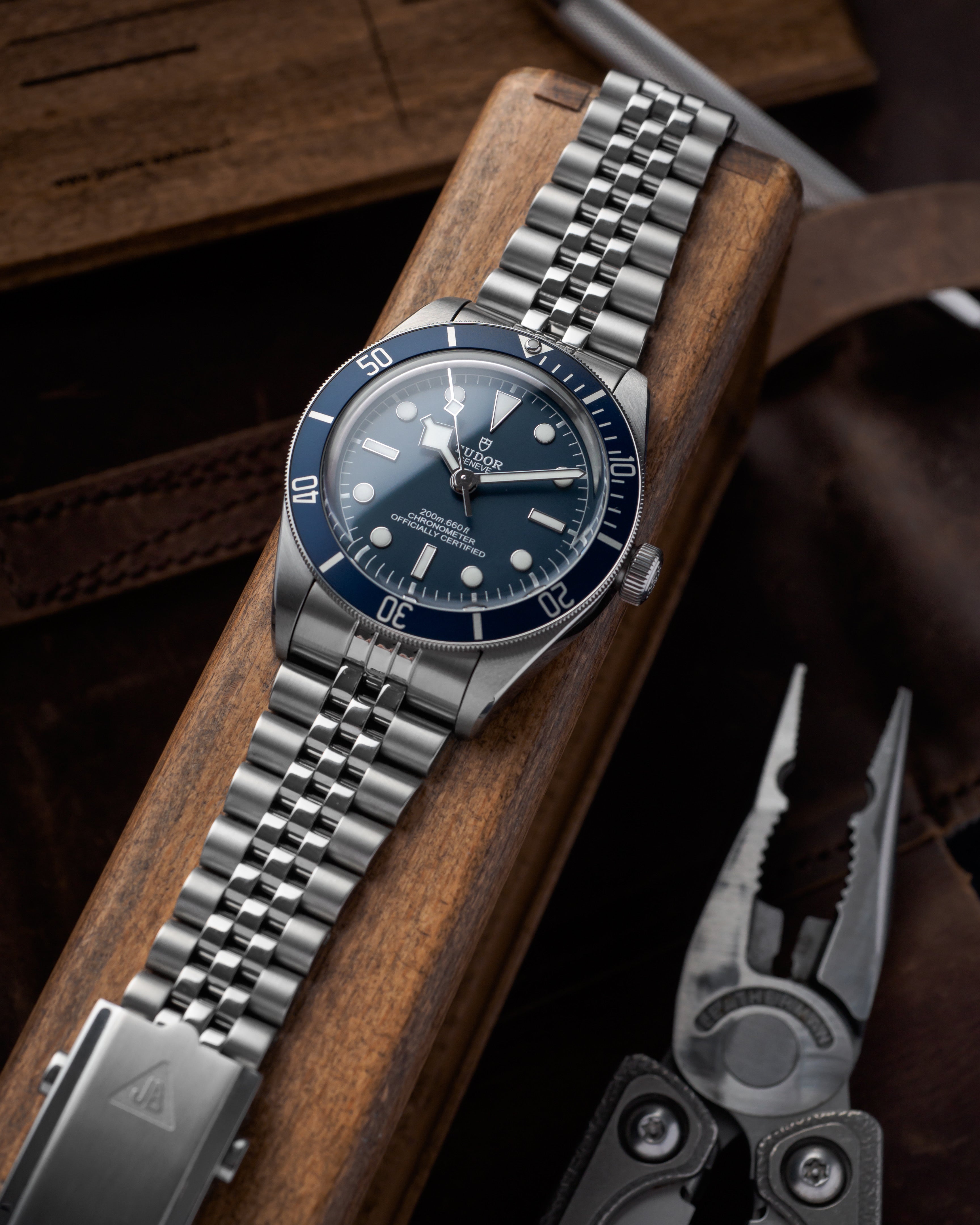 Stainless steel diving watch with navy blue bezel and dial on jubilee bracelet, displayed on wooden stand