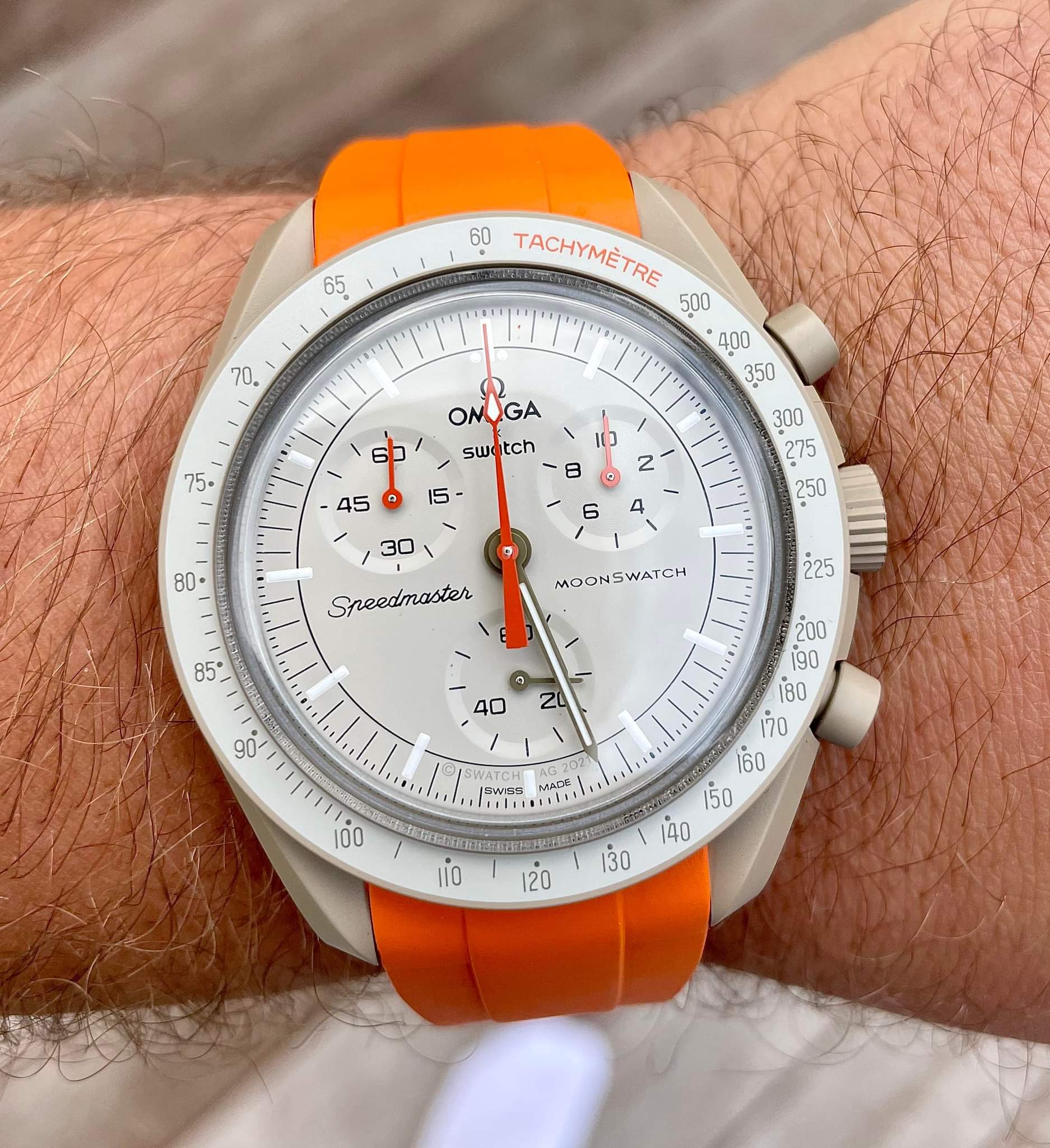 Omega Swatch Speedmaster Moonswatch white dial chronograph watch with orange rubber strap on wrist