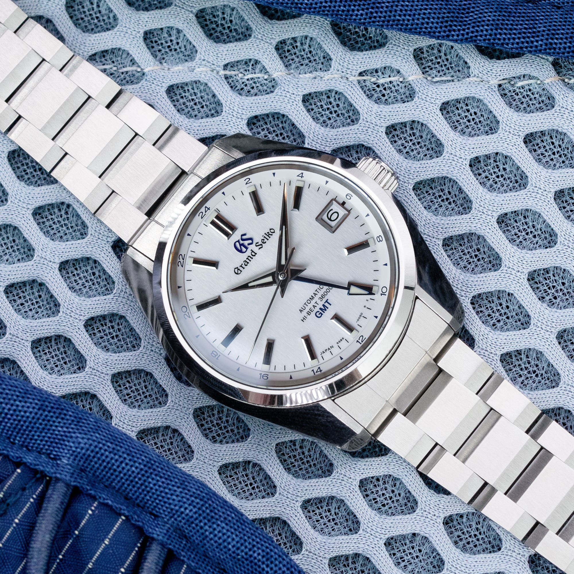 Grand Seiko GEMT automatic watch with white dial and stainless steel Hexad III bracelet on blue textile background