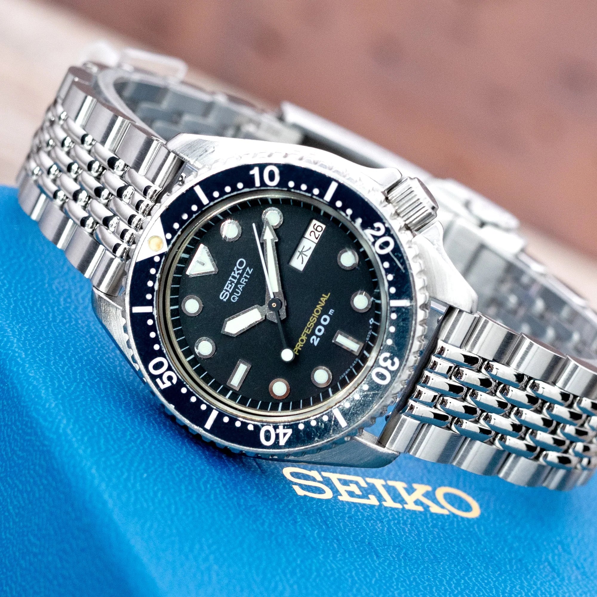 Seiko diver watch with stainless steel jubilee bracelet and black dial on blue background